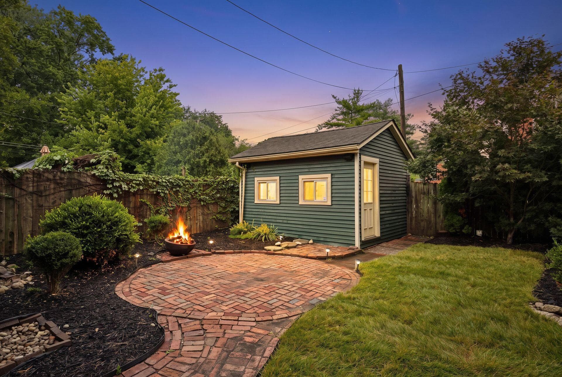 Detached structure with siding, brick paver patio, wood fencing, and landscape lighting