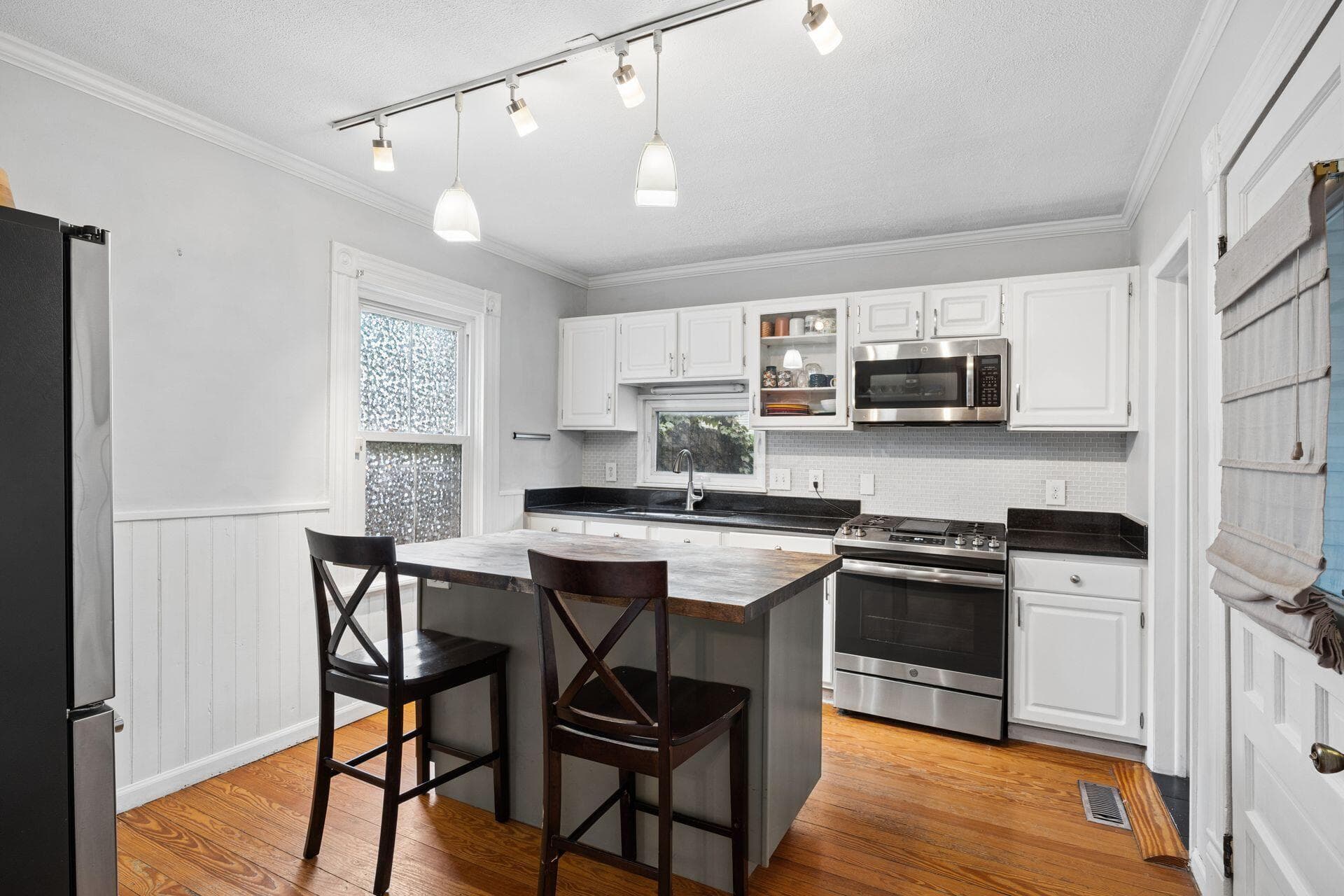 Kitchen featuring white cabinetry, dark countertops, stainless steel appliances, a center island with seating, and wood-finish flooring
