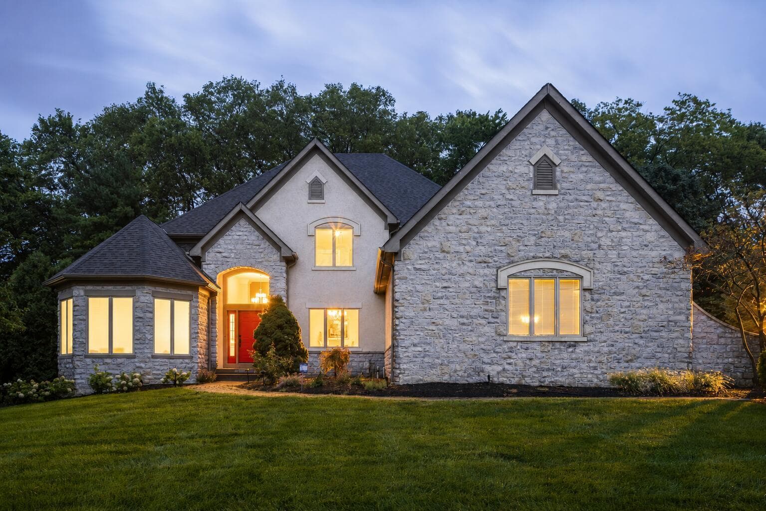 Beautiful twilight view showcasing the home’s distinctive architecture, mature trees and professionally landscaped setting.