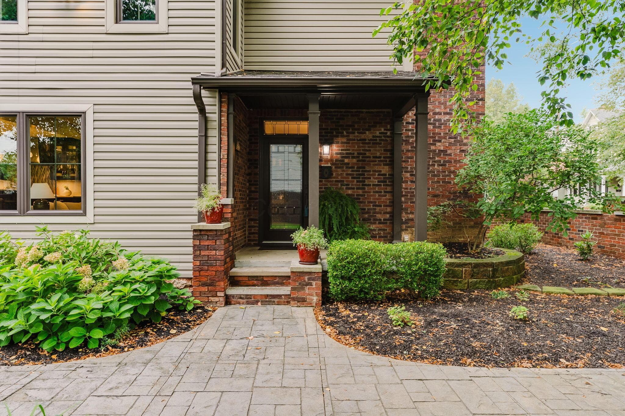 Brick and siding exterior featuring a covered entry, patterned concrete walkway, and mature landscaping