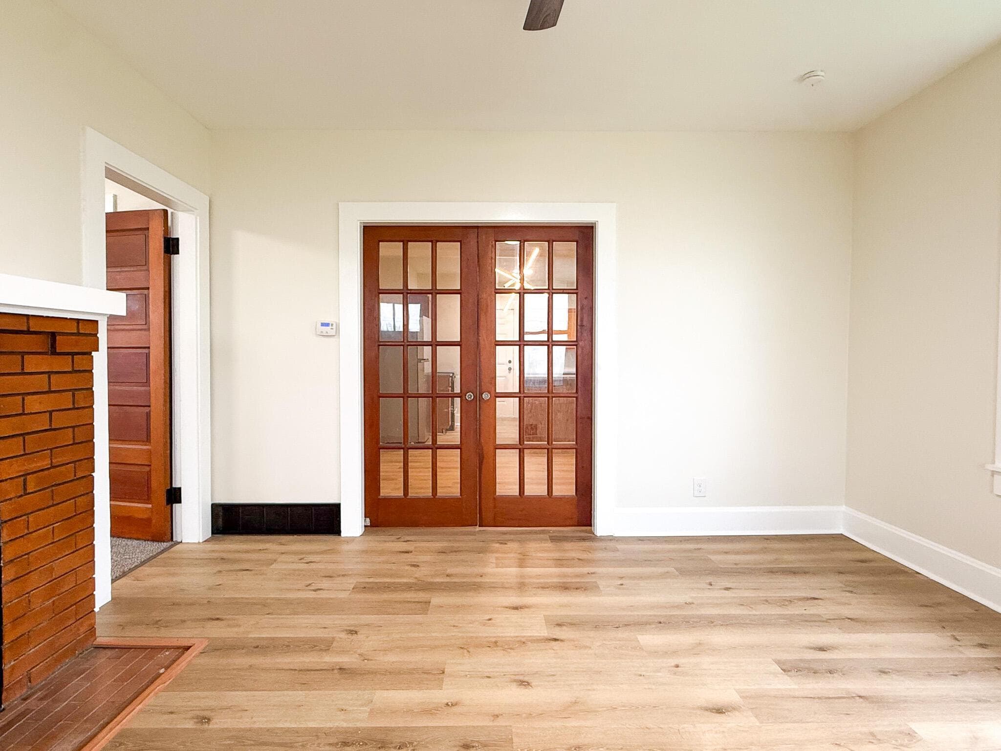 Light wood-finish flooring, white trim, red brick fireplace, and wood-paneled French doors