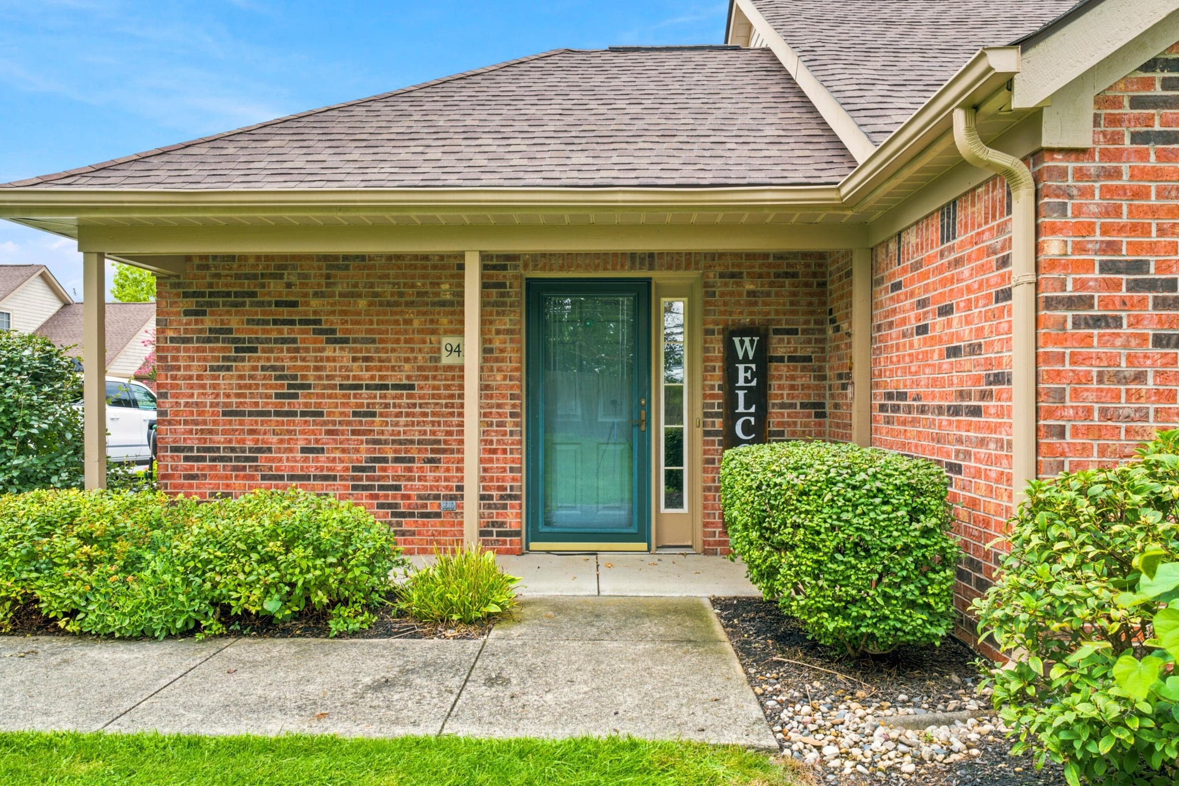 Brick facade with covered entry, concrete walkway, and established foundation plantings