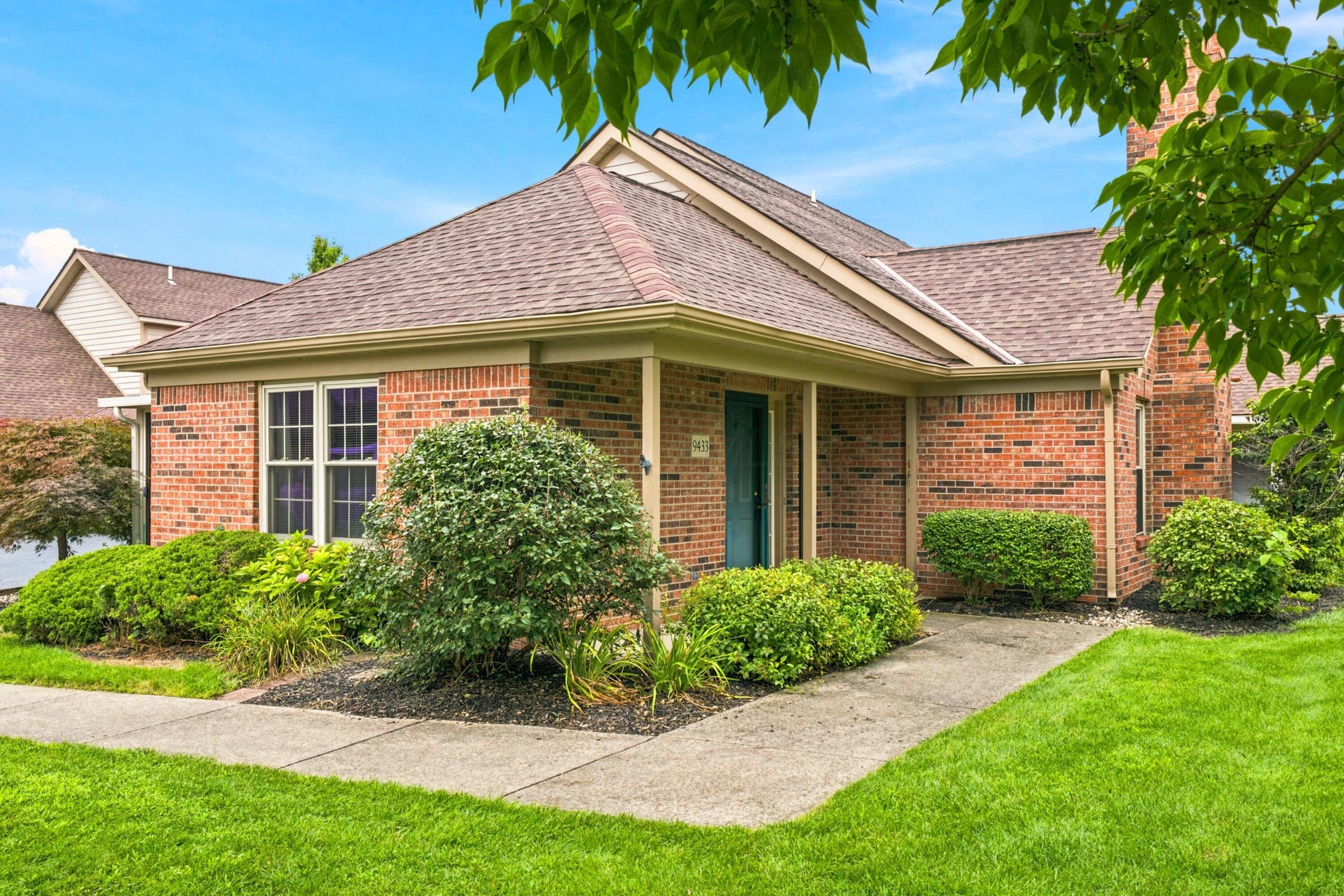 Charming brick home with a covered front portico, double-hung windows, and professional landscaping featuring manicured shrubs and lush lawn