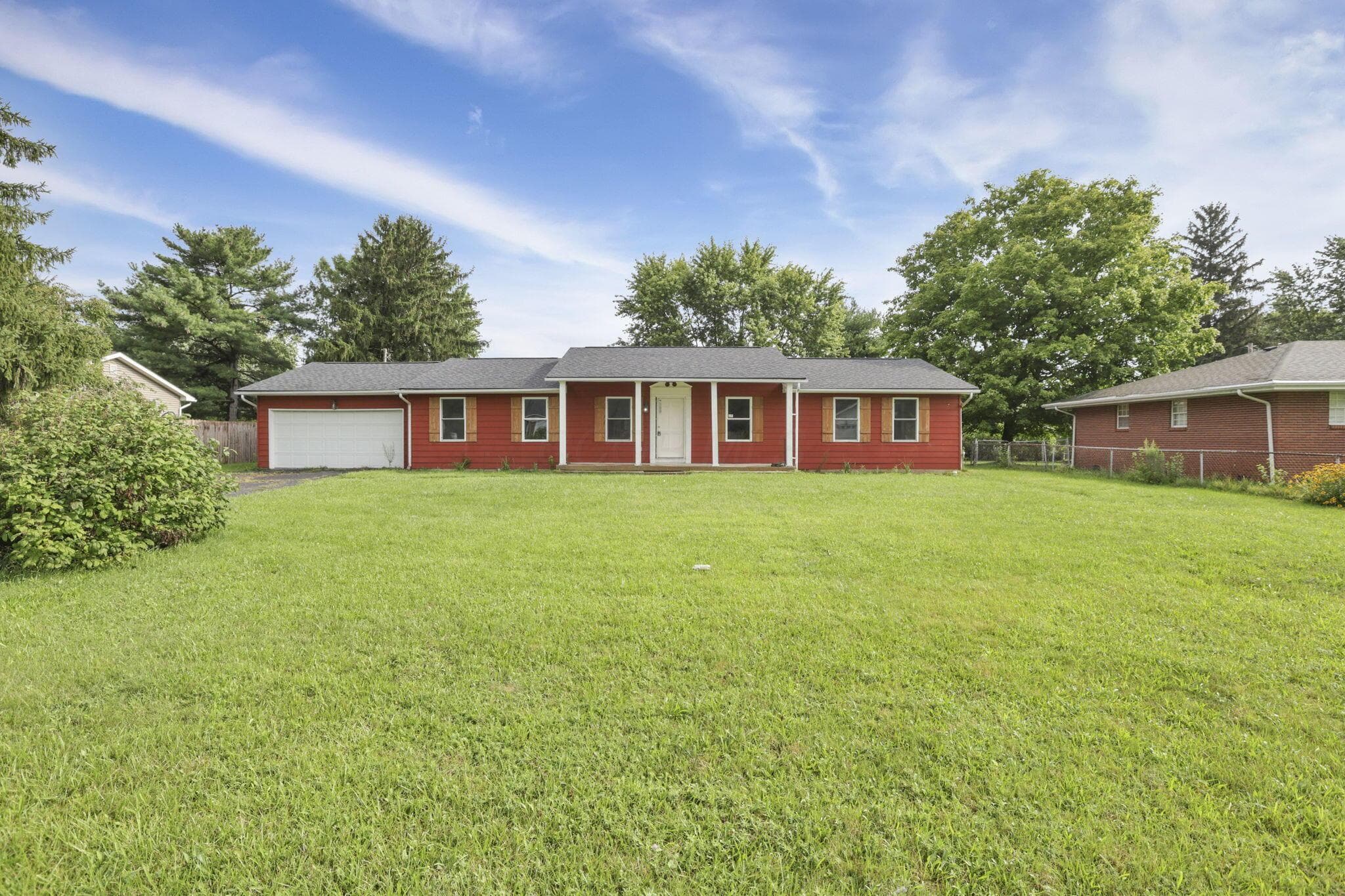 Brick ranch home situated on expansive grounds featuring a manicured lawn, mature landscaping, and an attached garage with white overhead door
