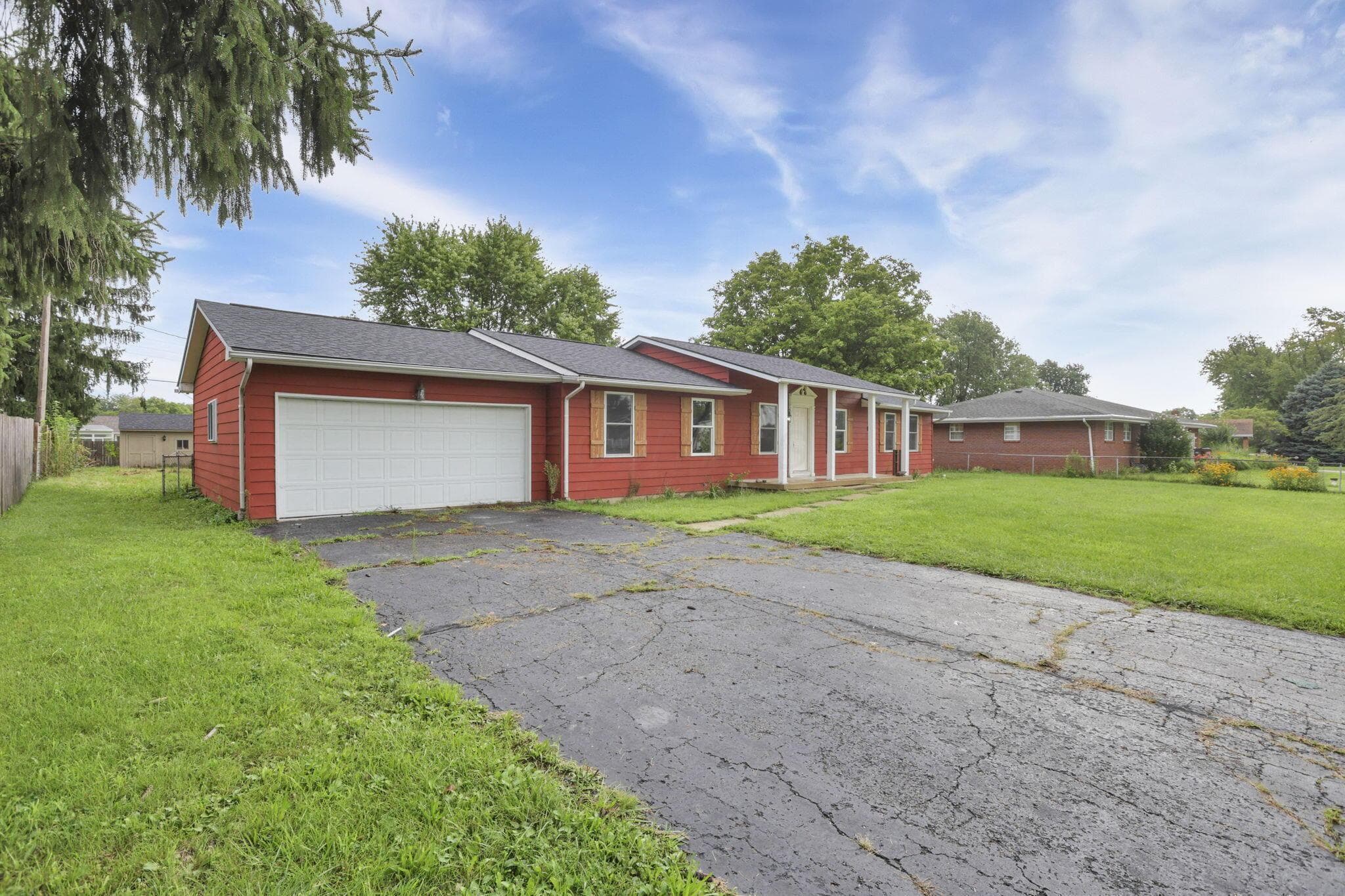 Ranch-style residence featuring a red siding exterior, a two-car garage, and a covered front entry