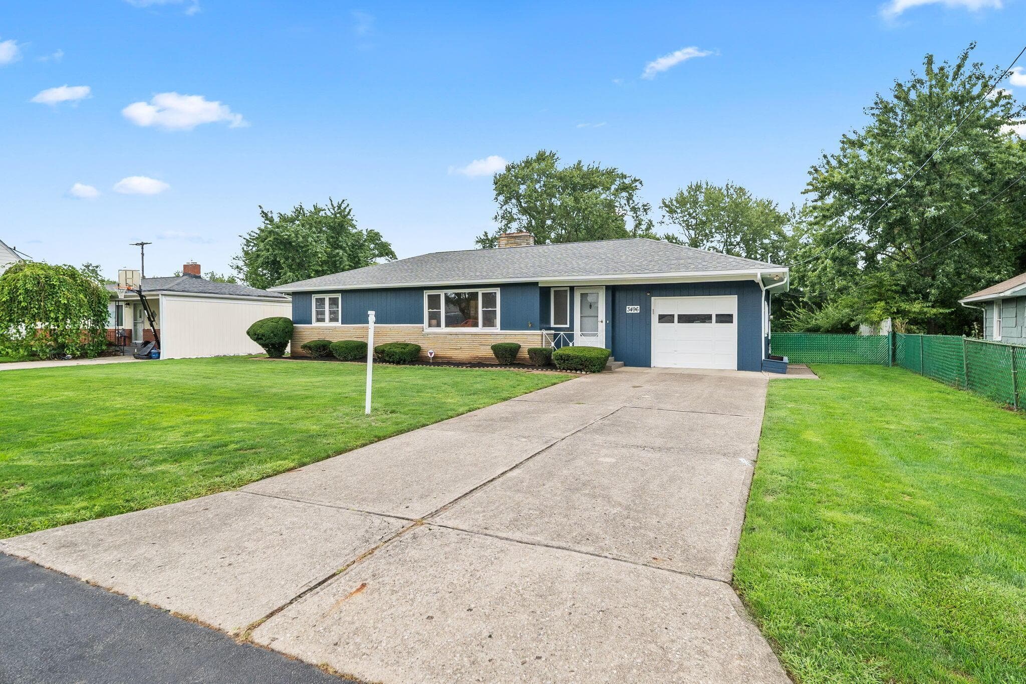 Blue siding exterior with a white garage door, concrete driveway, and a front lawn with mature landscaping