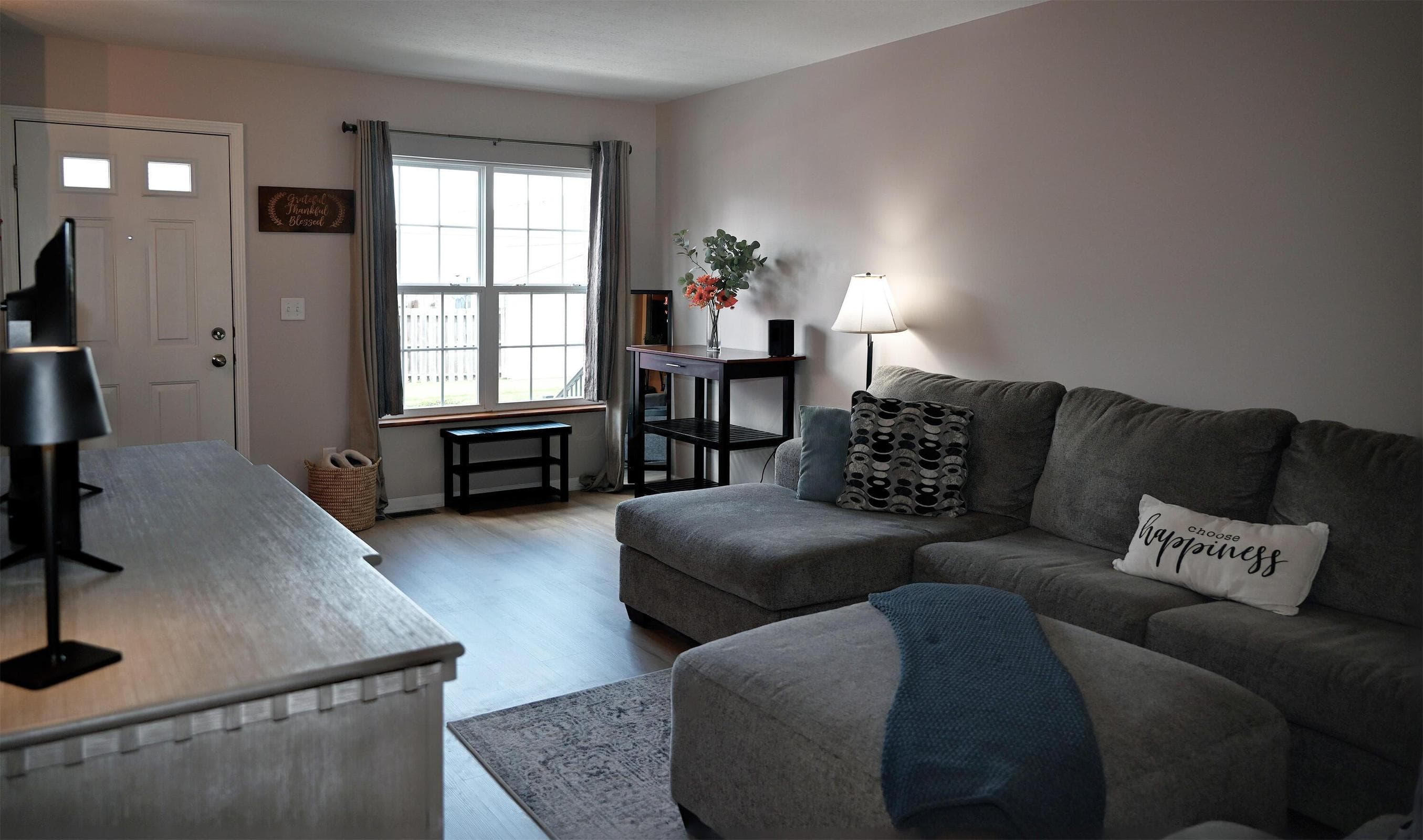 Bright and inviting living room featuring luxury vinyl plank flooring, large front-facing window, neutral décor, and an open layout ideal for relaxing or entertaining.