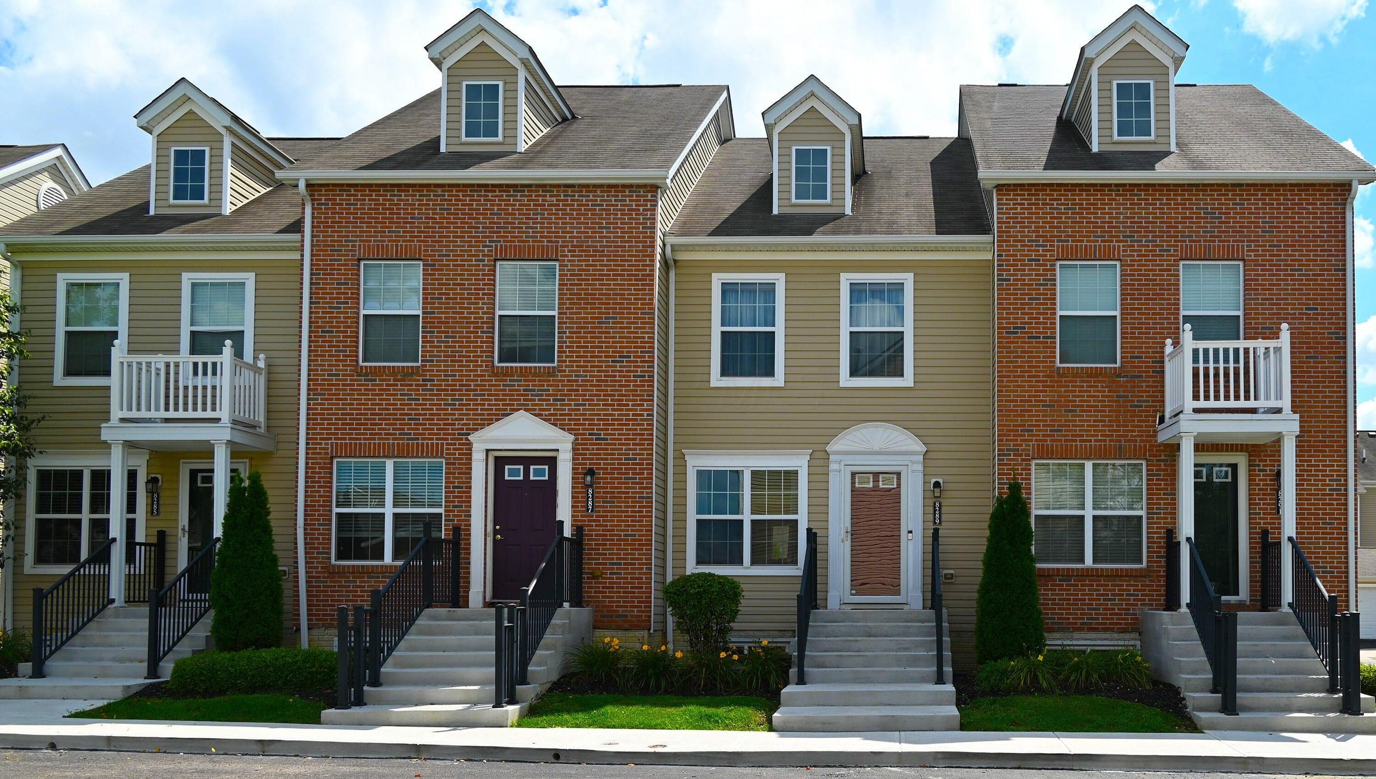 Exterior view of the four-unit building featuring the subject property. Attractive brick and siding façade with individual private entrances, architectural detailing, and professionally maintained landscaping.