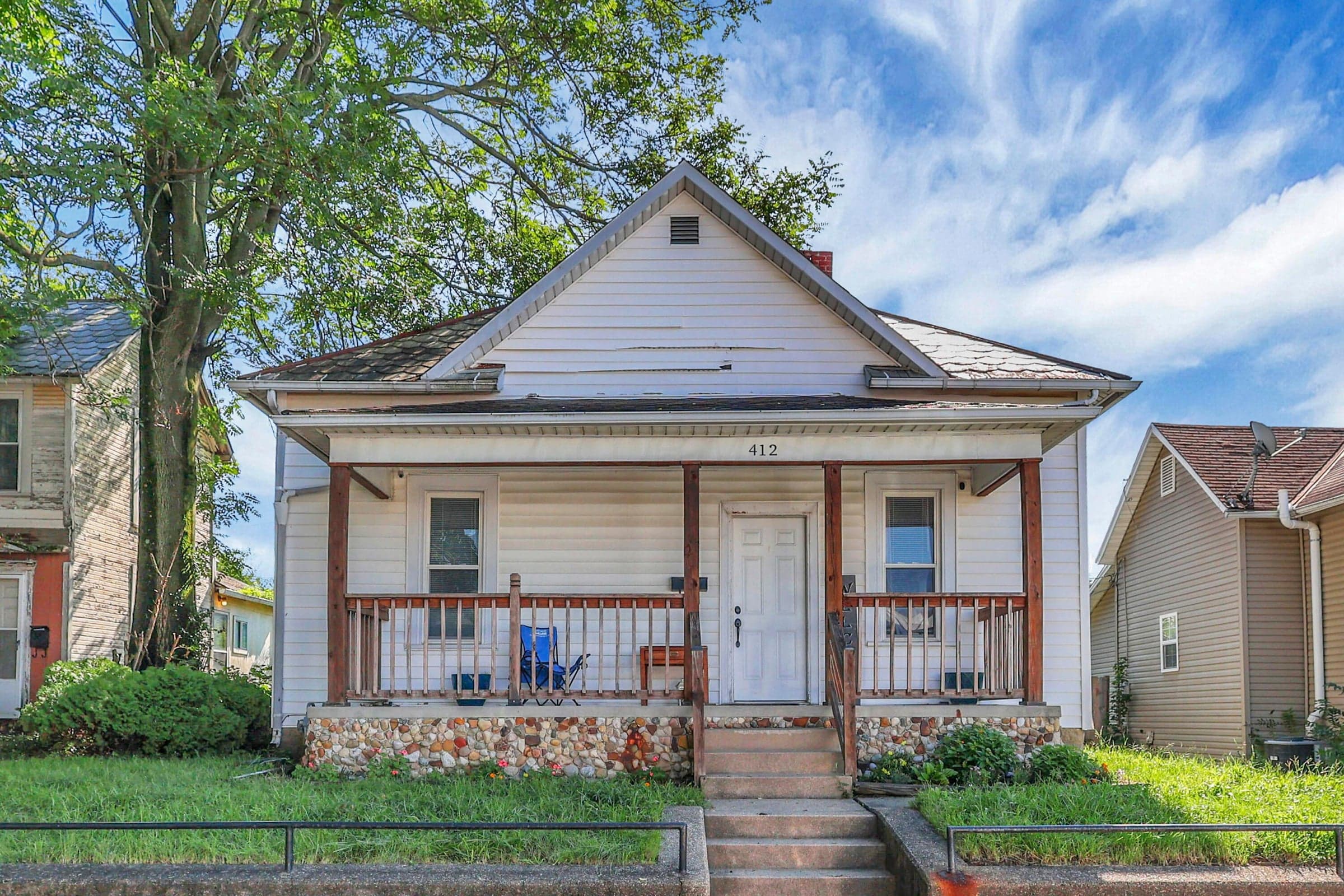 White siding exterior with a covered front porch, wood balusters, and a stone foundation