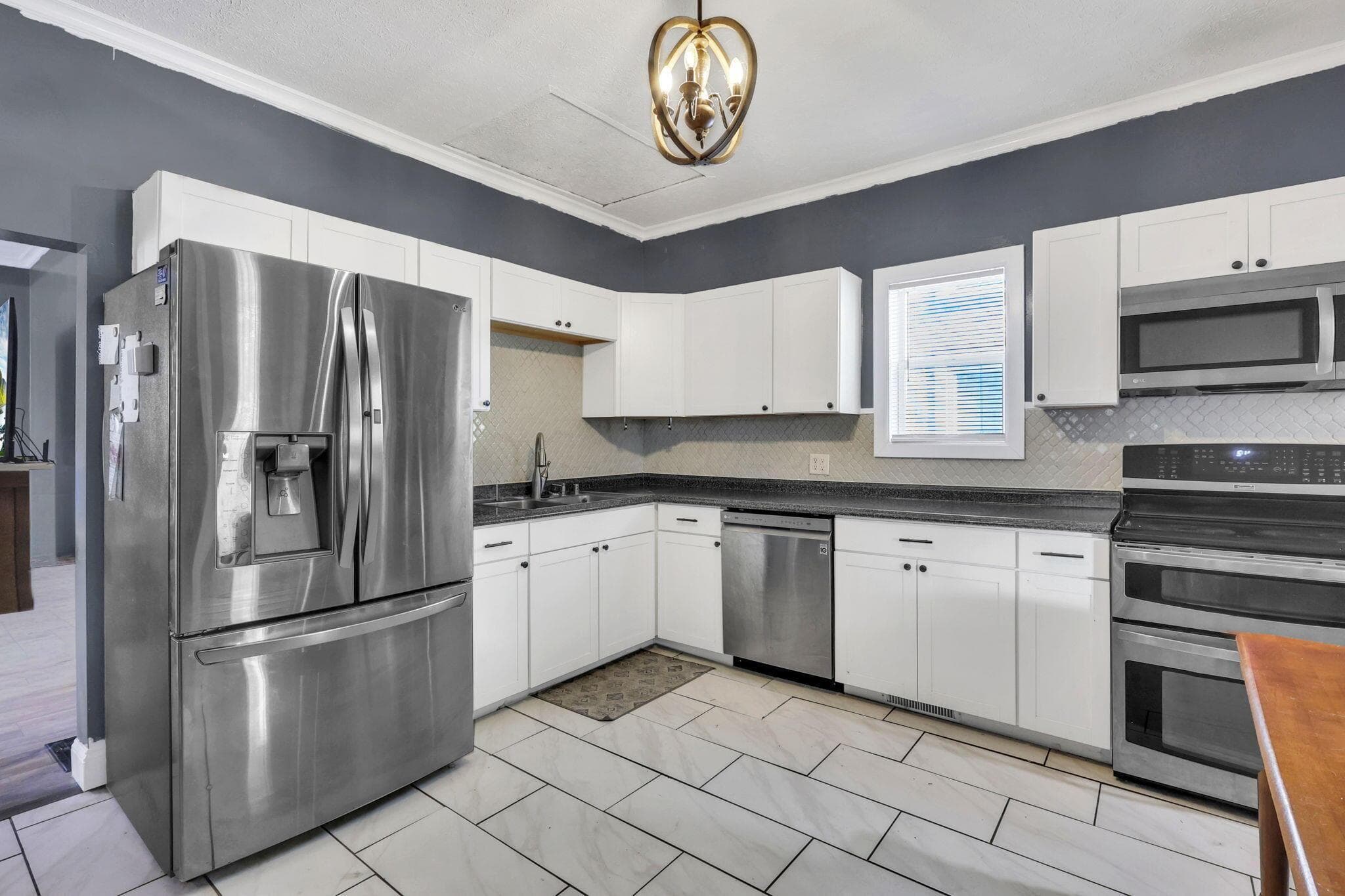 White shaker-style cabinetry, stainless steel appliances, dark countertops, tile flooring, and a decorative ceiling fixture