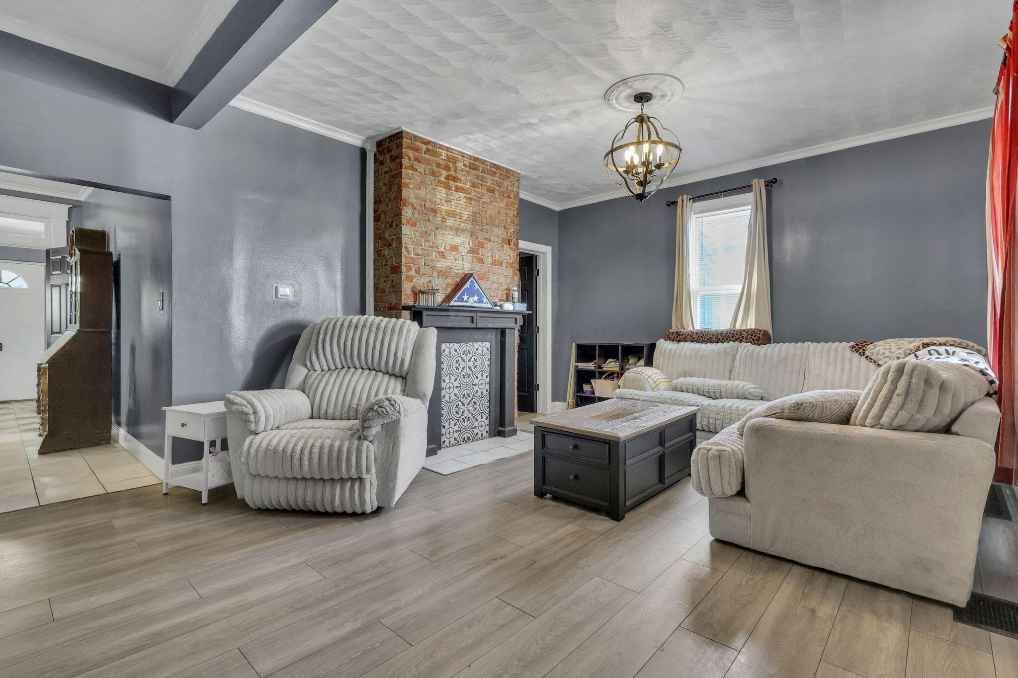 Wood-finish flooring throughout, brick accent wall, decorative fireplace surround, ceiling medallion, and ornate chandelier