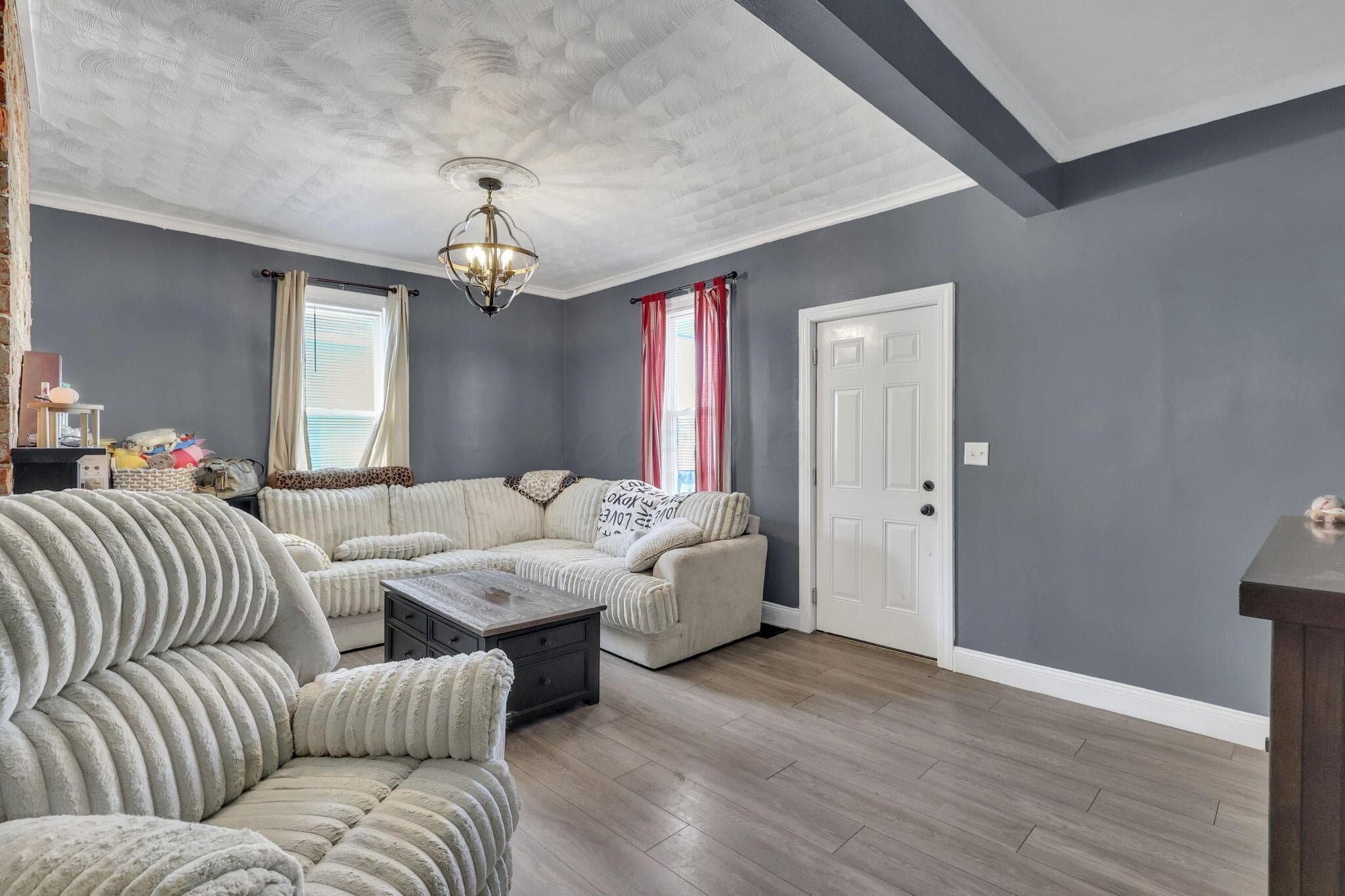 Wood-finish flooring, accent ceiling beams, contemporary chandelier, crown molding, and two windows providing natural light