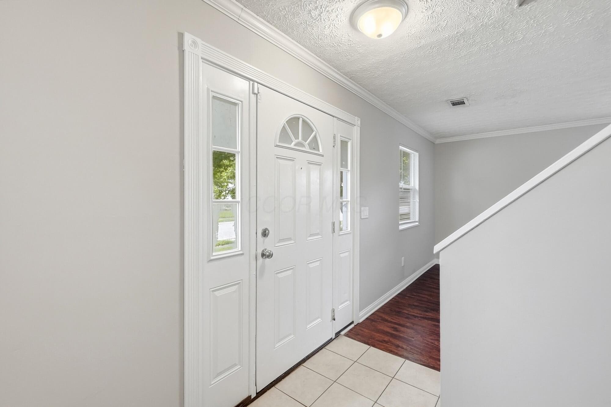 Entryway featuring a white paneled door with an arched transom, sidelights, and light-colored tile flooring