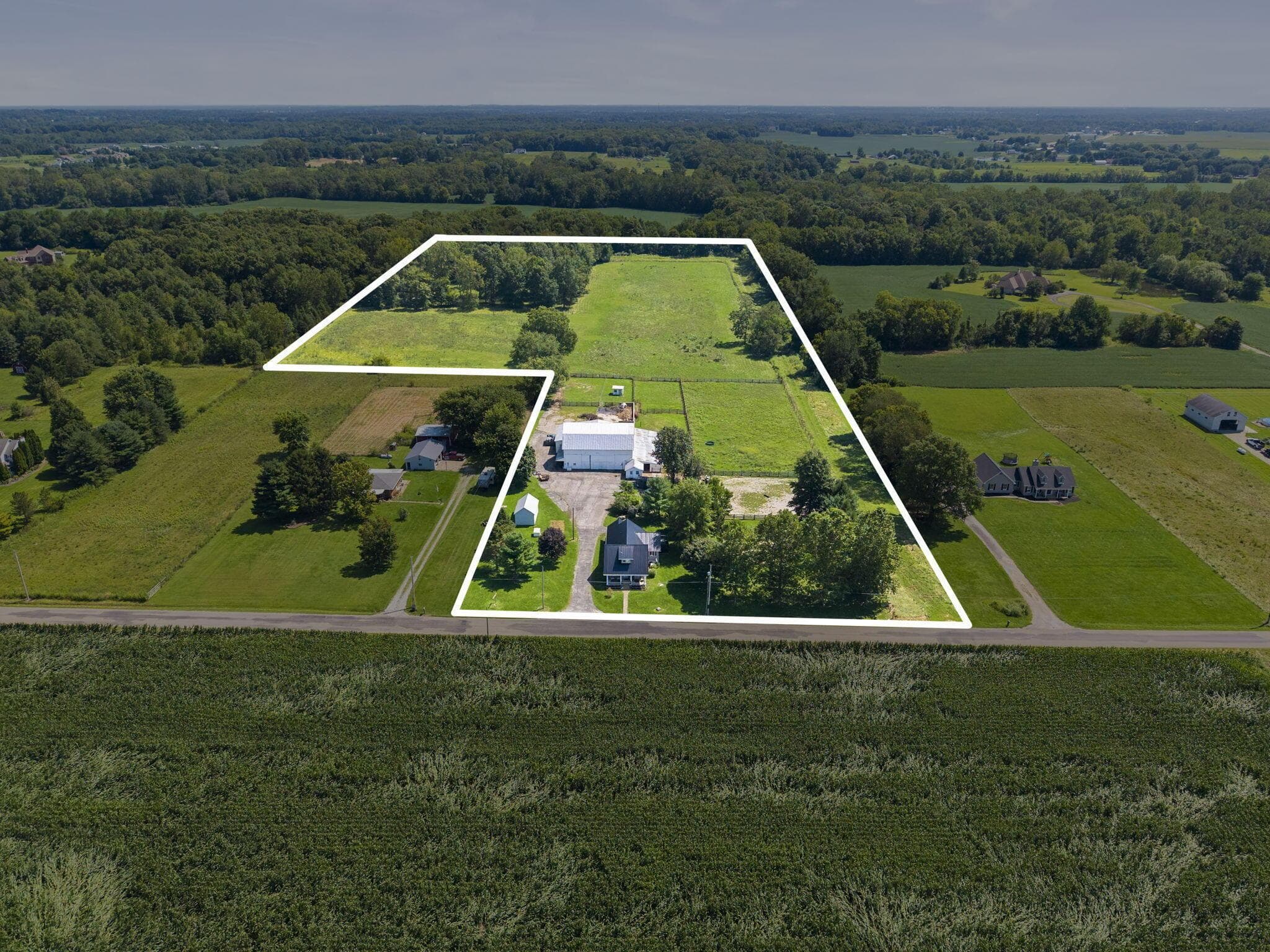 Expansive rural property featuring a primary residence, a large outbuilding, a smaller accessory structure, and extensive open fields