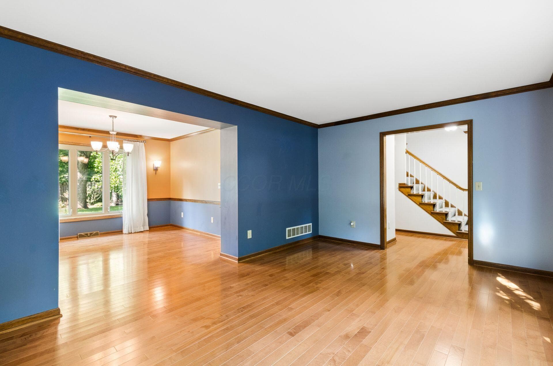 Hardwood flooring throughout, crown molding details, large window with natural light, built-in staircase with wood railing, and a chandelier in the dining area