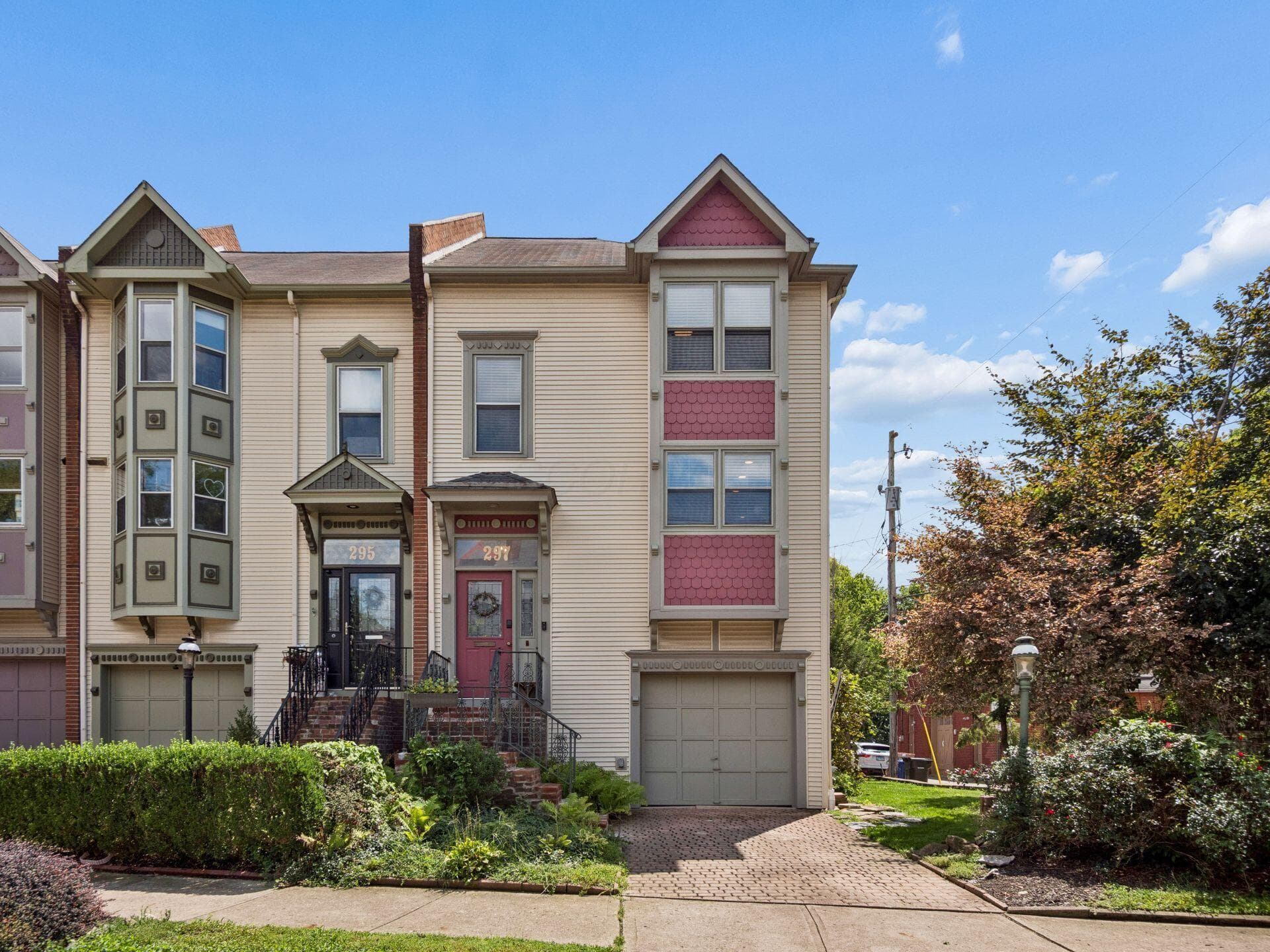 Multi-story townhouse featuring a gabled roofline, decorative bay window, front entry porch, and an attached garage with a paved driveway