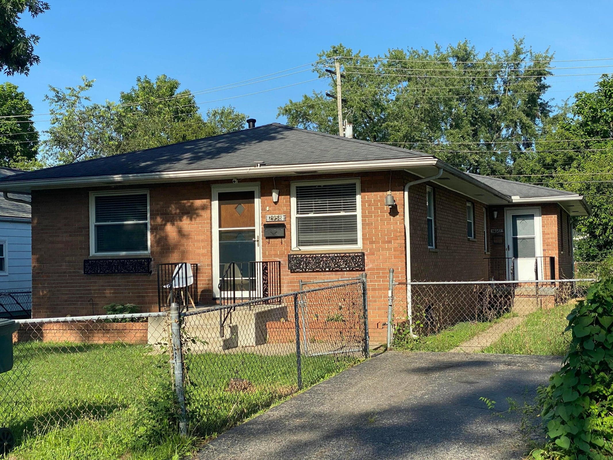 Brick exterior with a dark shingle roof, chain link fencing, a rear parking space of alley.