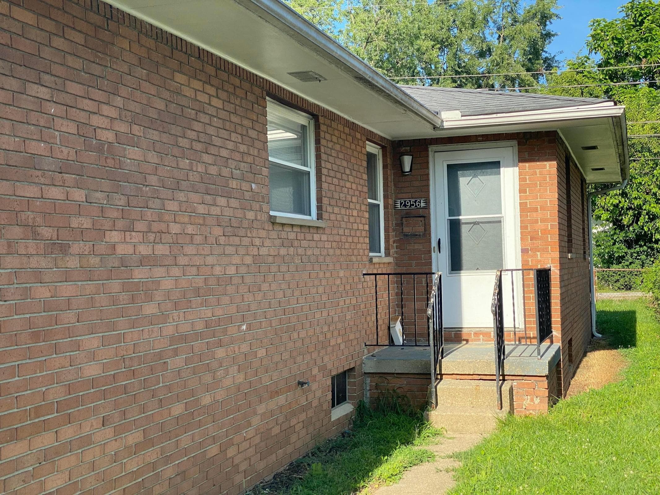 Brick exterior with white trim, covered entry, front door with storm door, and metal handrails