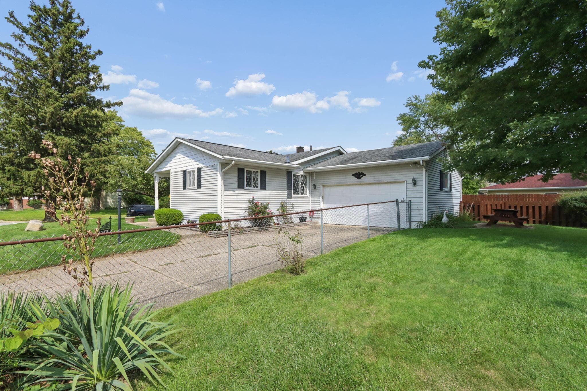 Siding exterior with a covered porch, attached garage, and a chain-link fence