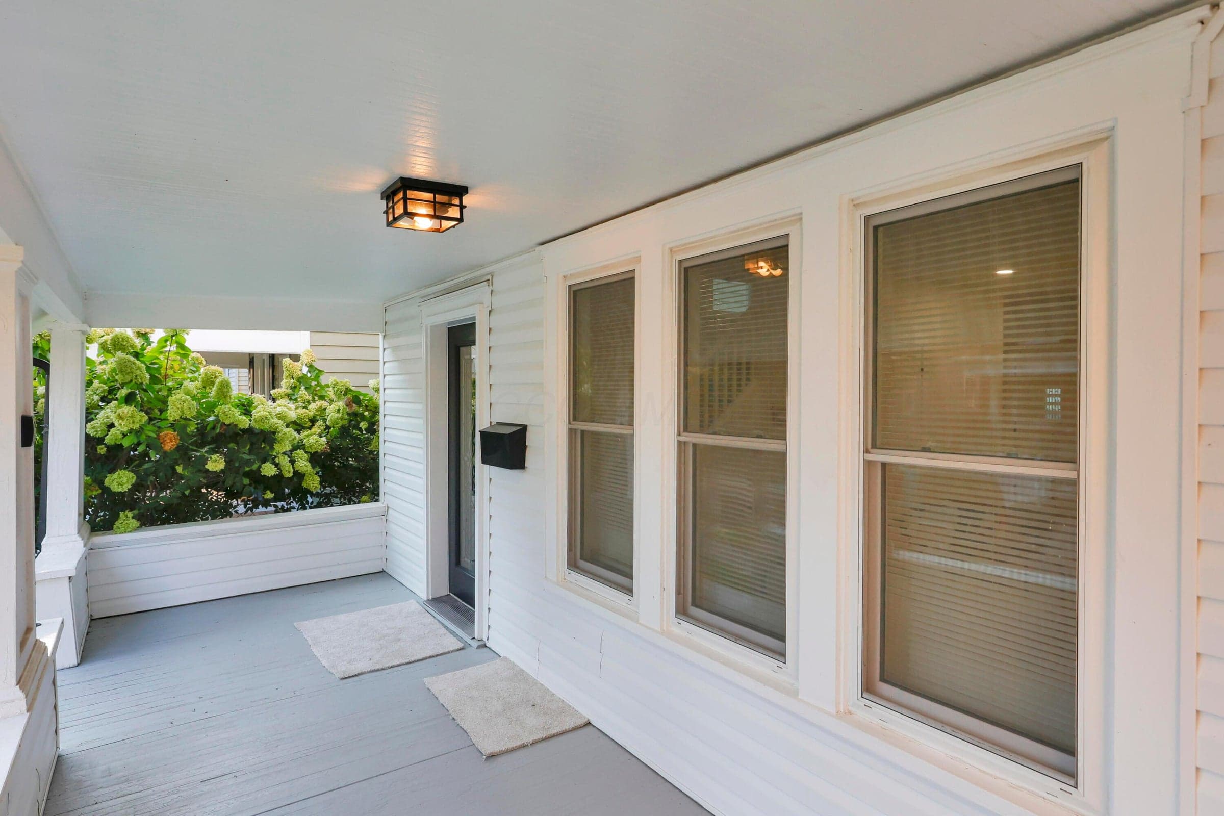 Covered porch with painted flooring, white shiplap siding, and a flush-mount ceiling light