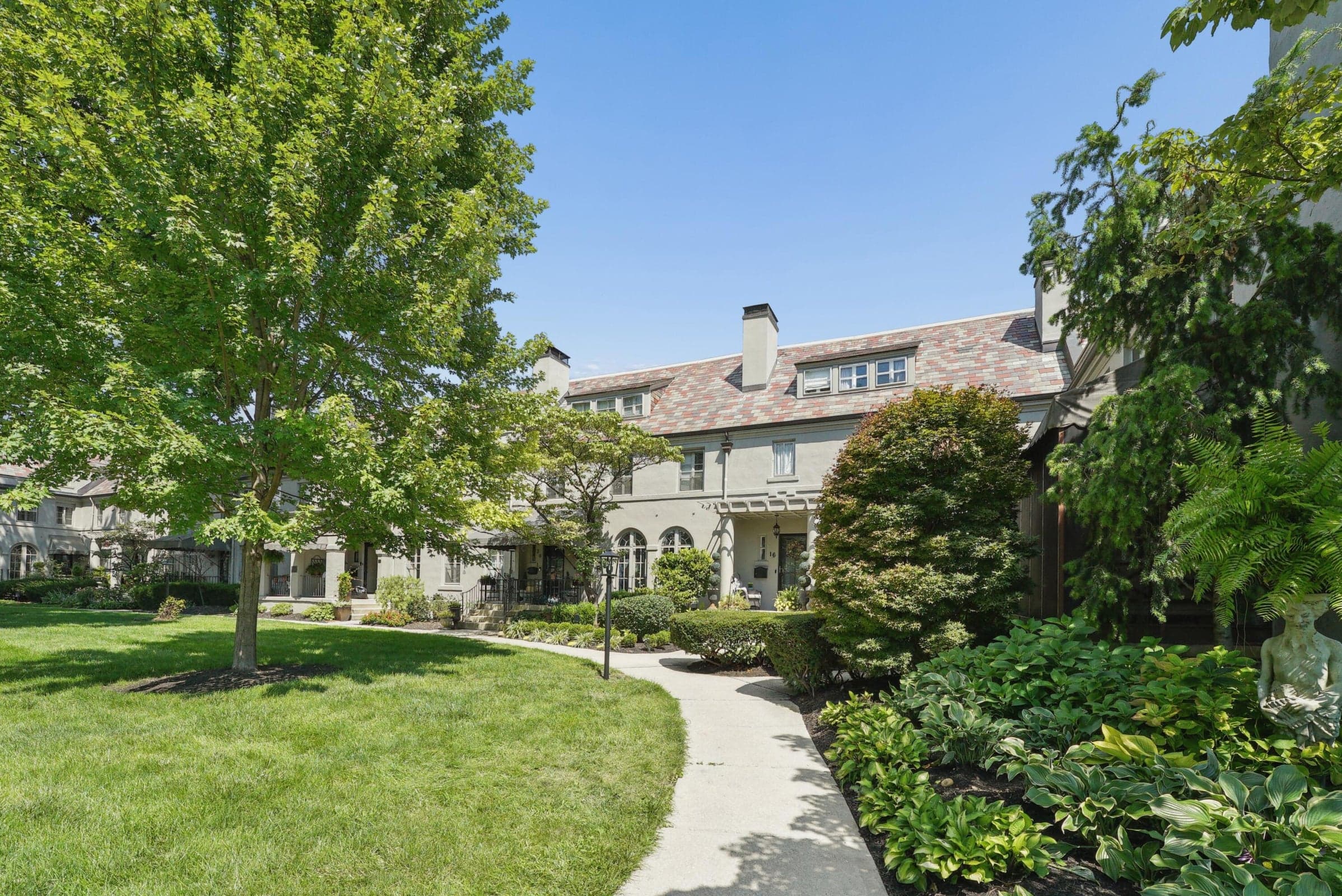 Manicured lawn with mature trees, established landscaping, and a winding paved pathway