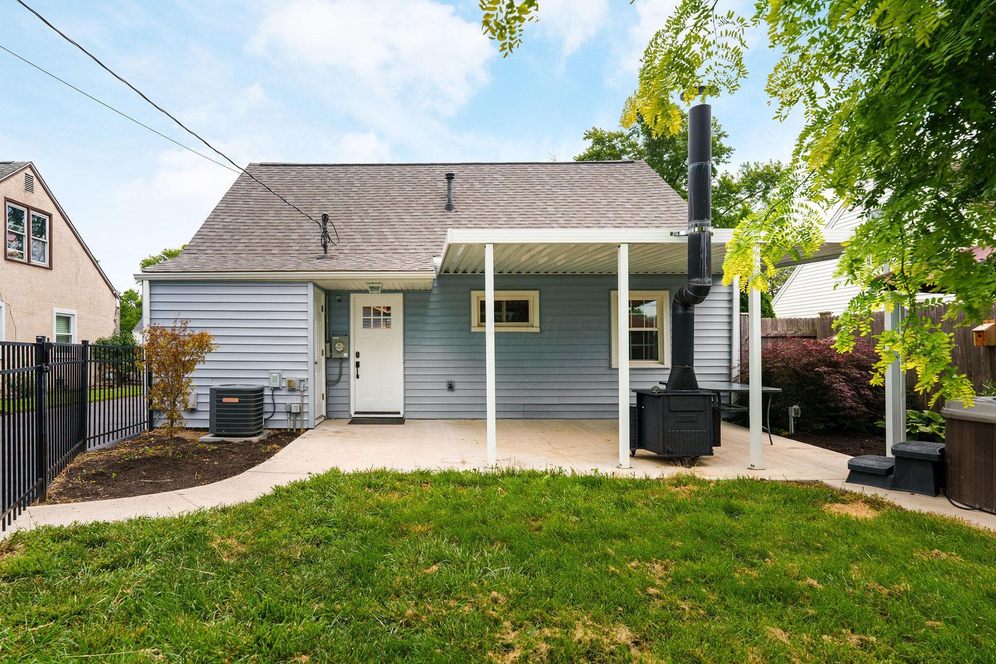 The back of the home with covered concrete patio with woodburning stove inside the beautifully landscaped yard.