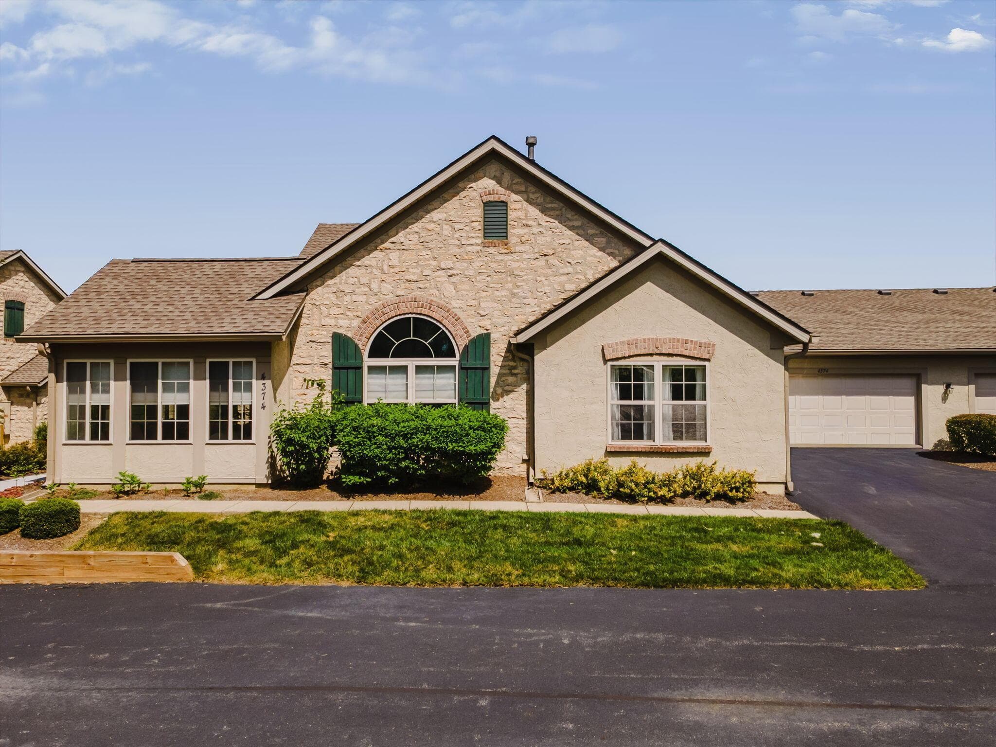 Stone and stucco facade with a shingle roof, arched window with shutters, and an attached garage