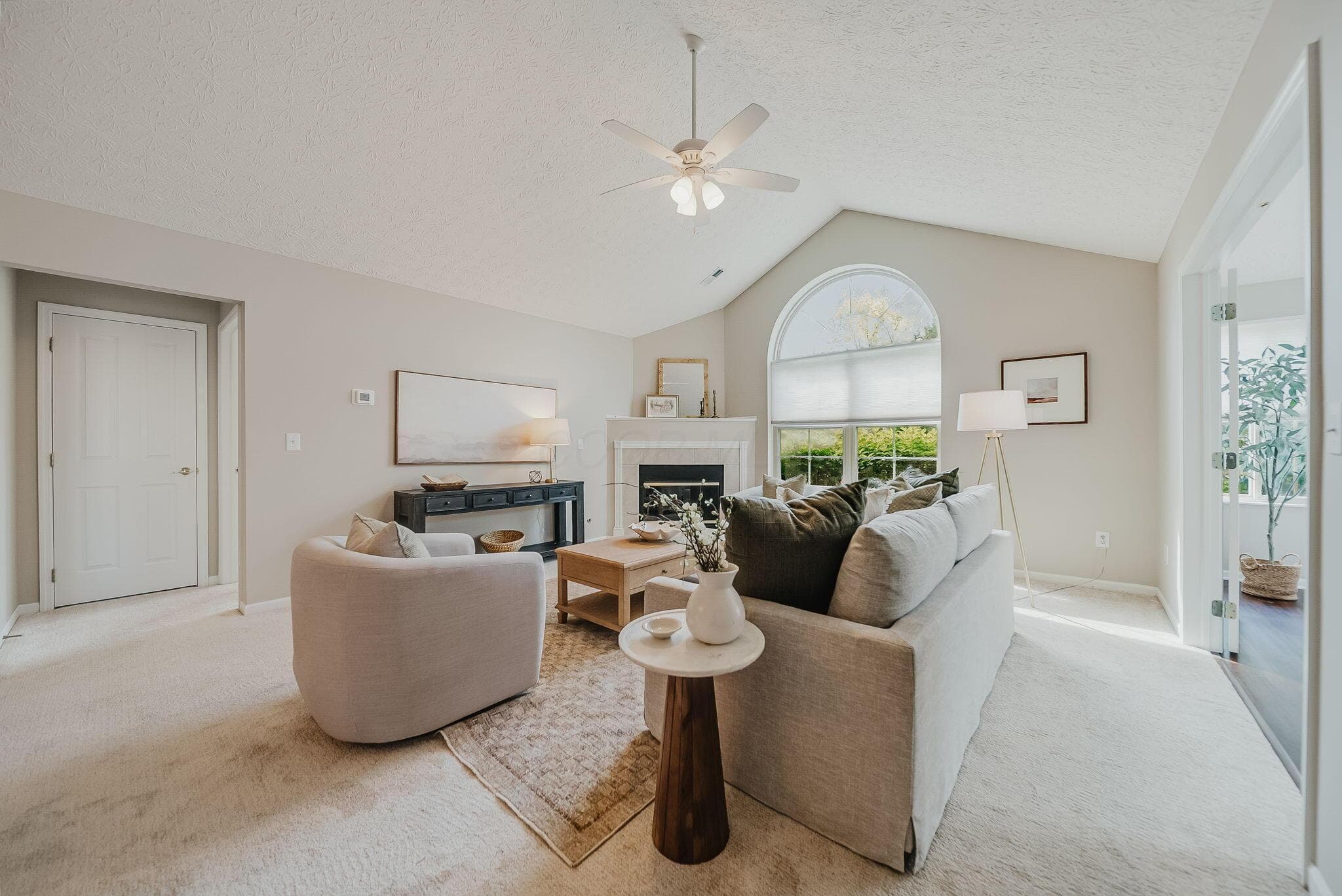 Vaulted ceiling with ceiling fan, arched window, fireplace with mantel, and light-toned carpeting