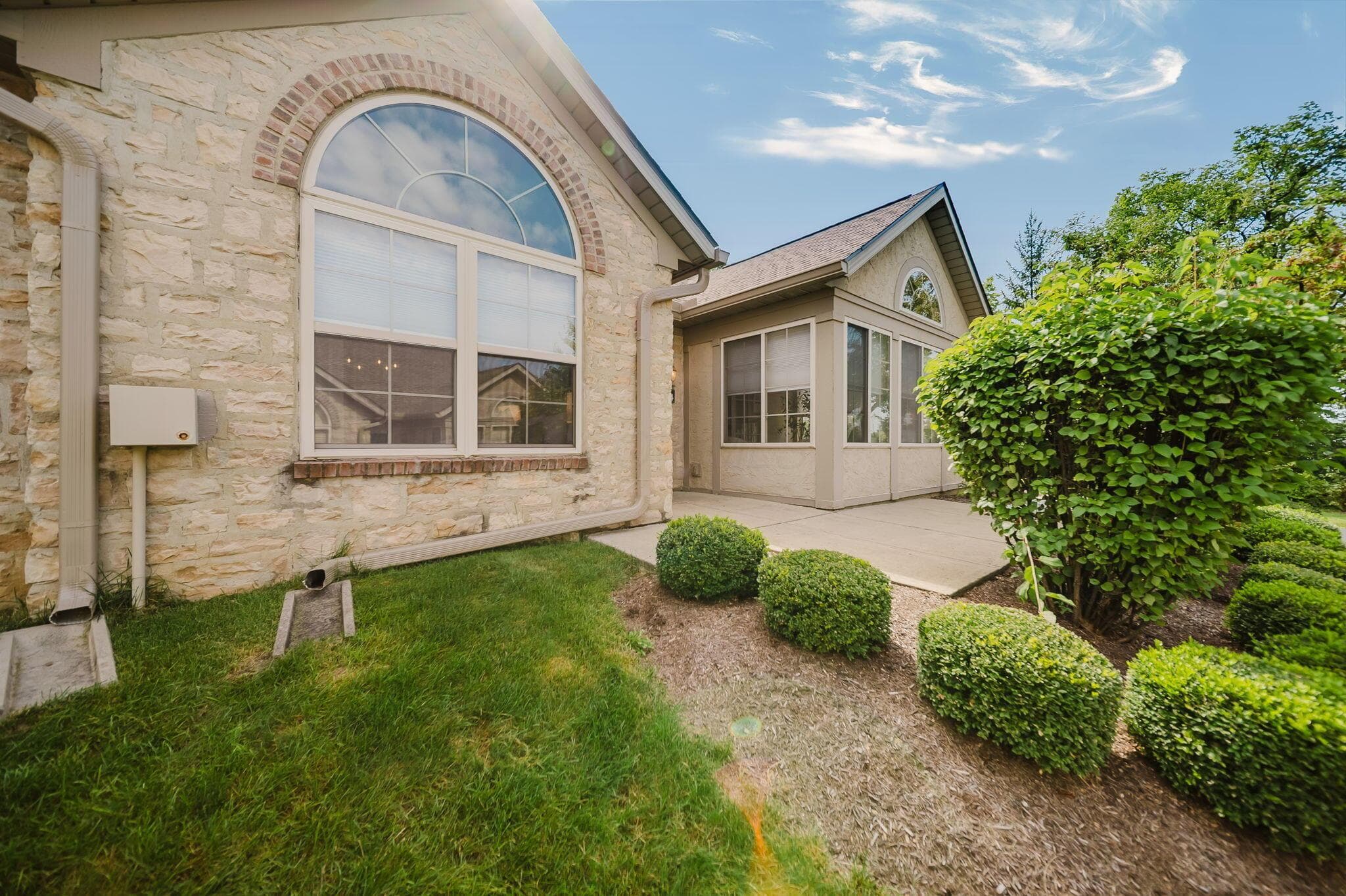 Stone exterior with an arched window, a screened-in porch, and a concrete patio