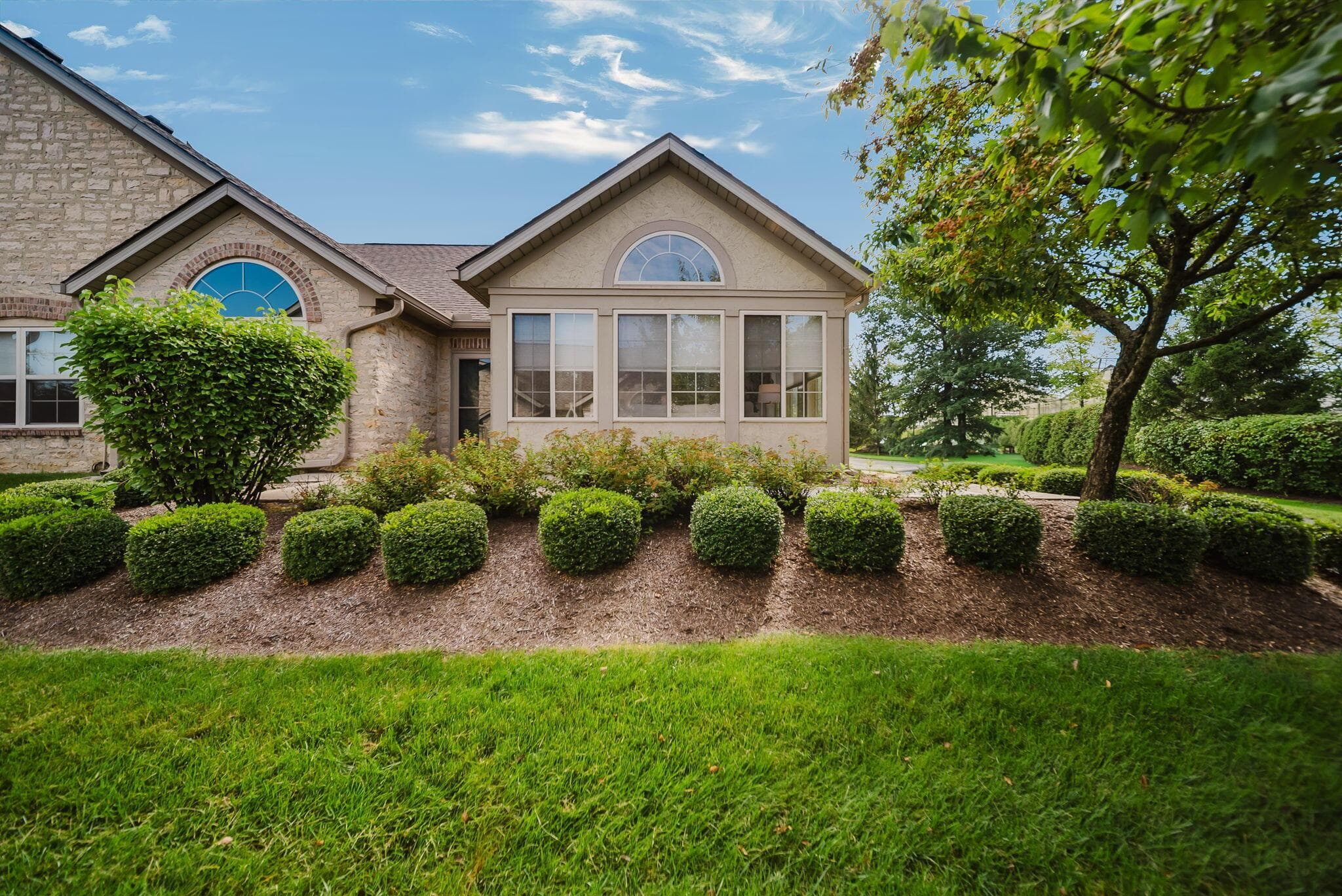 Stone and stucco exterior with arched transom windows and a sunroom with multiple windows