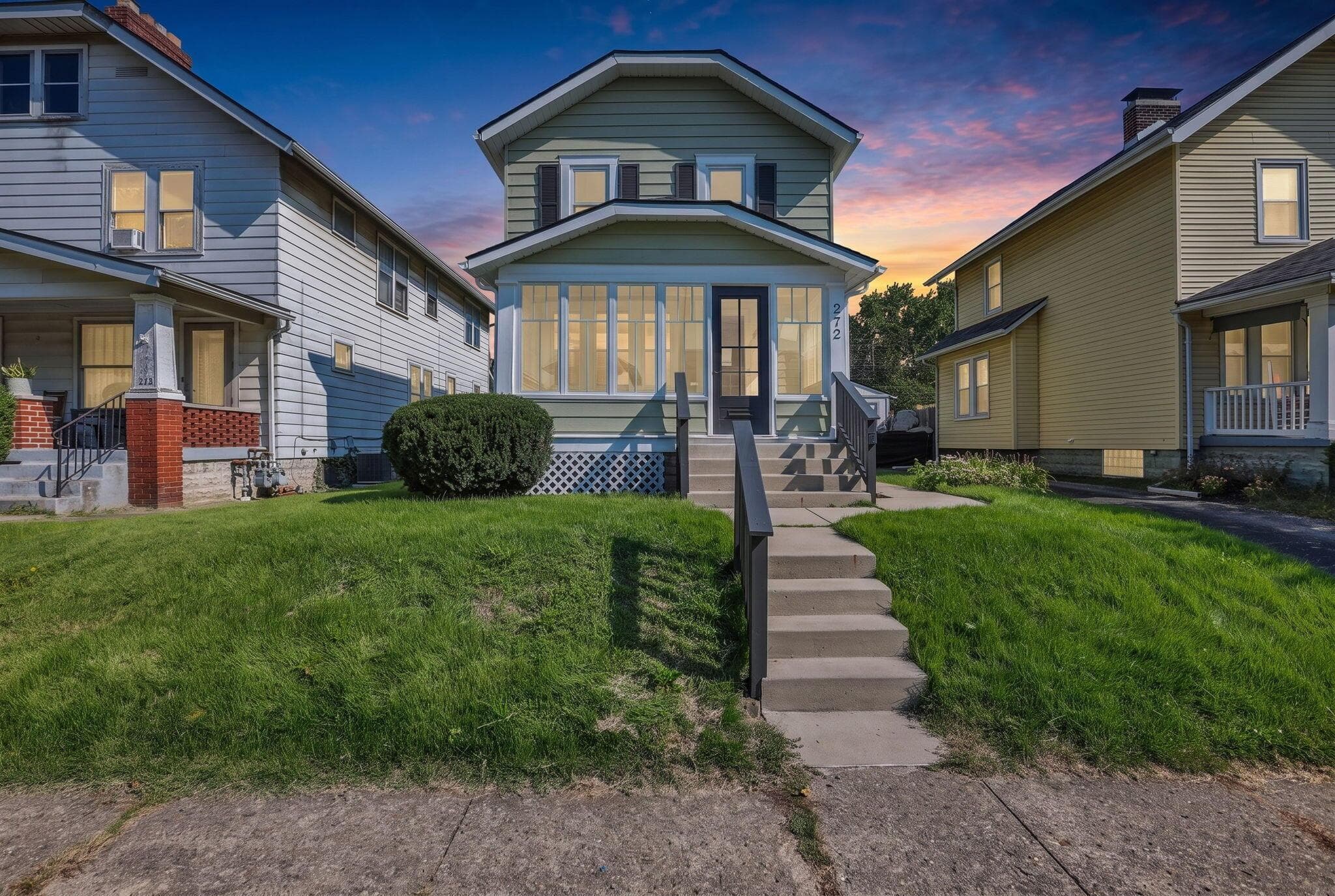 Two-story exterior with siding, enclosed porch, concrete steps, and a front yard with mature shrubbery