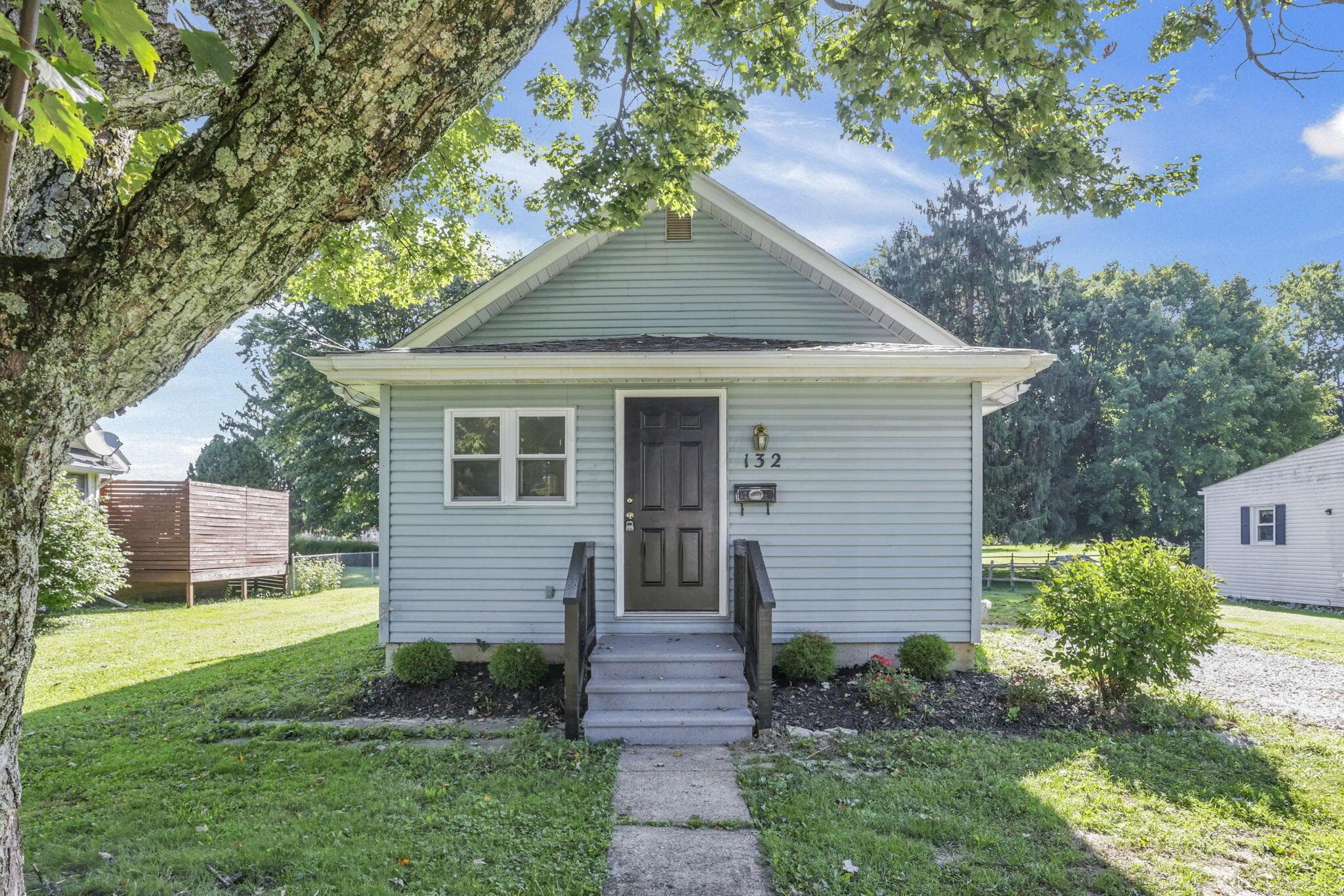 Light blue siding exterior with a dark front door, white trim windows, and a paved walkway