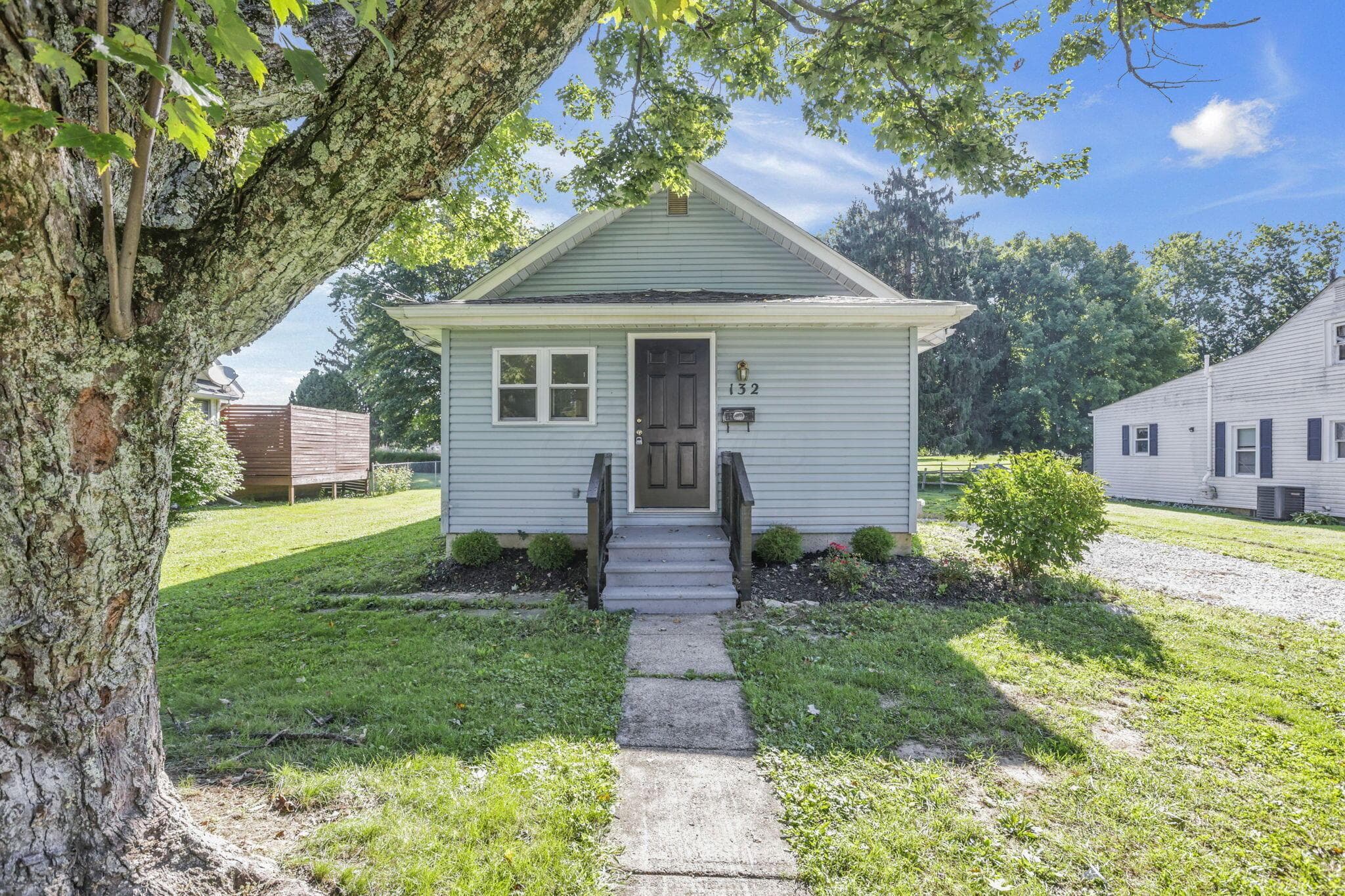 Light blue siding exterior with a dark-colored entry door, concrete steps, and a front yard