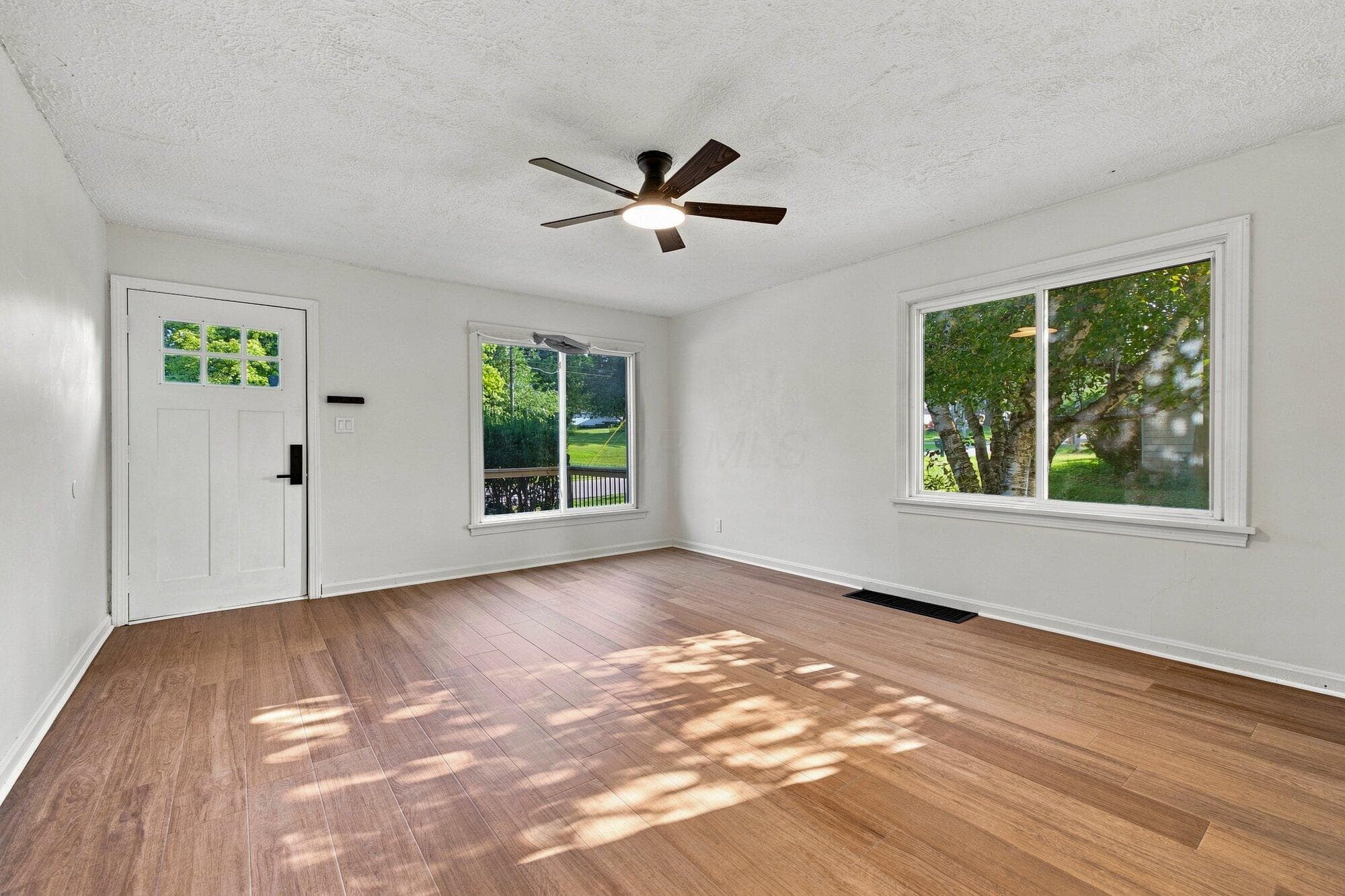 Wood-finish flooring, white paneled door with divided lite window, ceiling fan with integrated lighting, and white-framed windows
