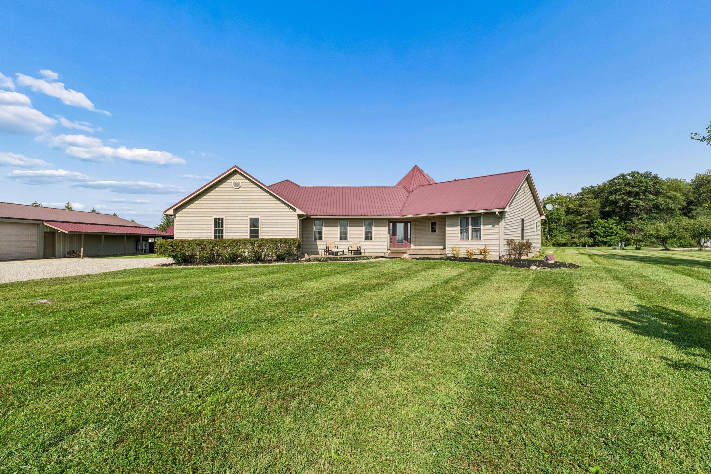 Expansive green lawn, Clay siding exterior, burgundy metal roof, covered front entry, and detached garage