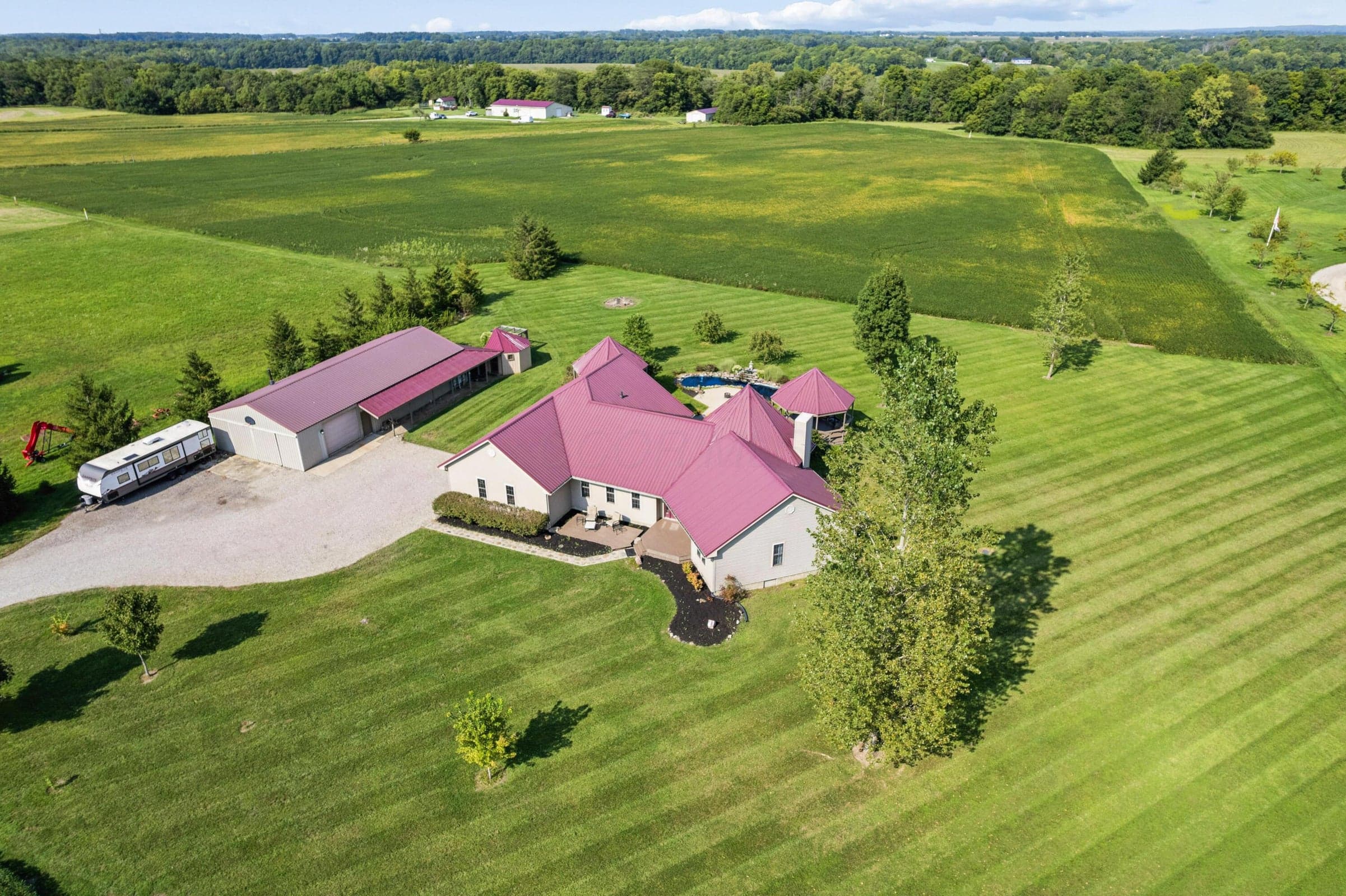 Expansive property featuring a residence with a metal roof, a detached pole barn with a metal roof, a gravel driveway, and established landscaping