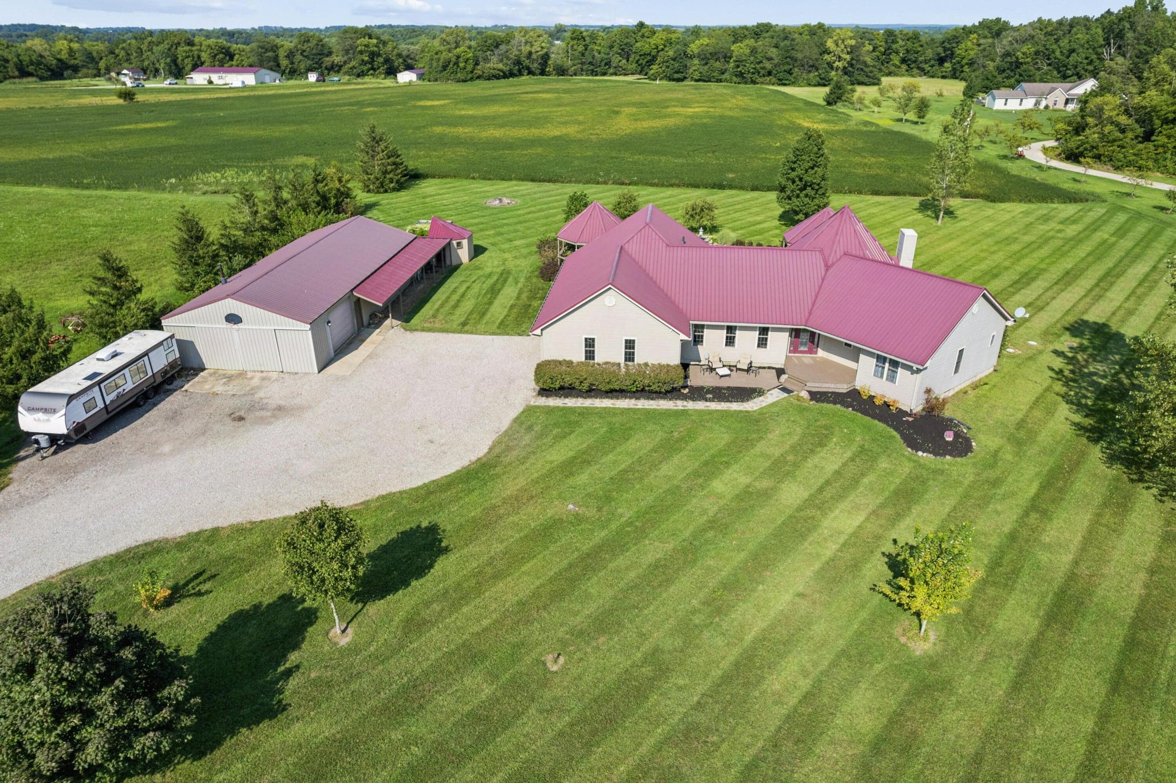 Expansive green lawn surrounds a single-story residence with a burgundy metal roof and an accompanying large detached pole barn