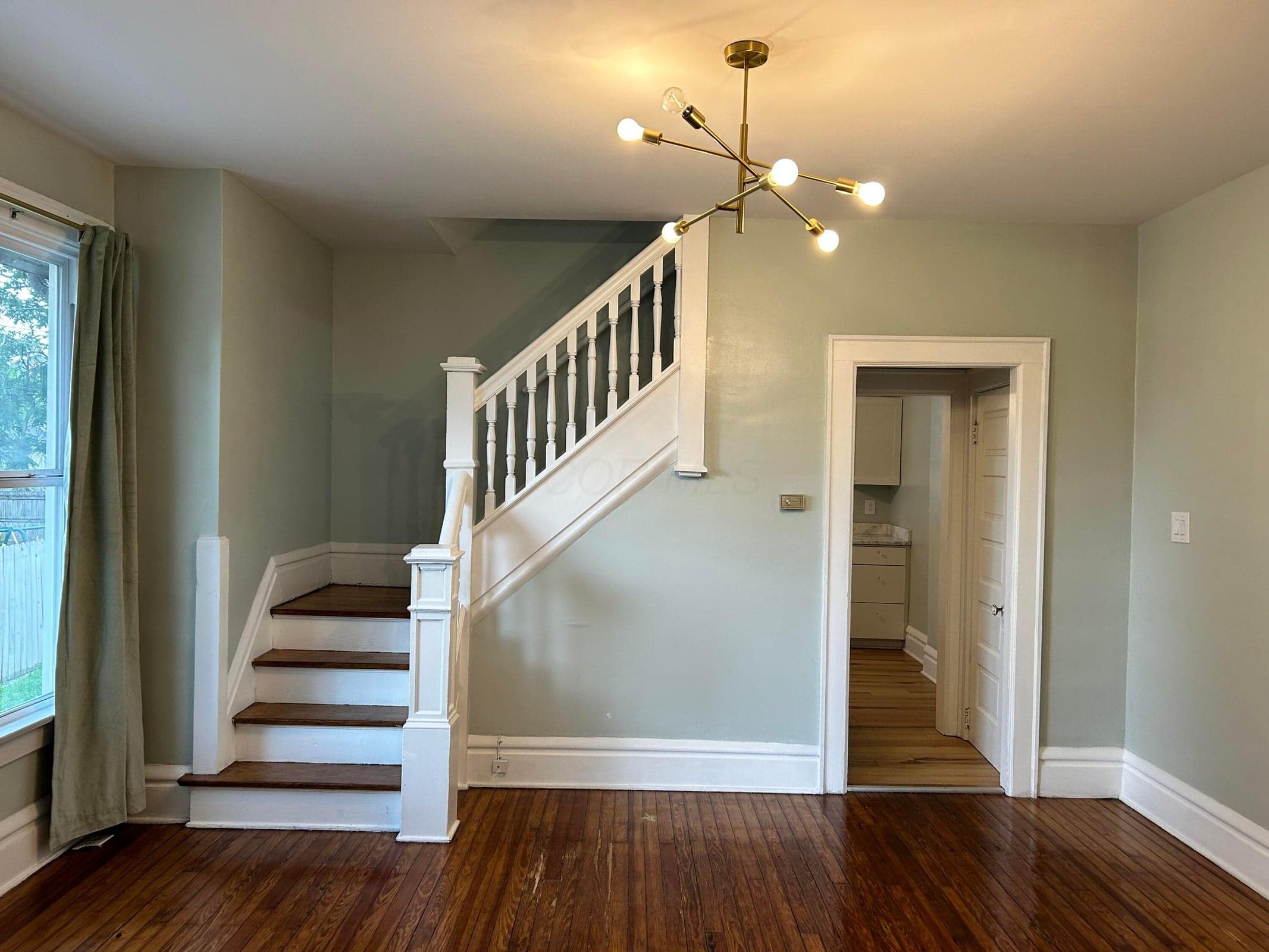 28- Hardwood flooring, painted staircase with white balusters, contemporary ceiling fixture, cased doorway, and window with trim
