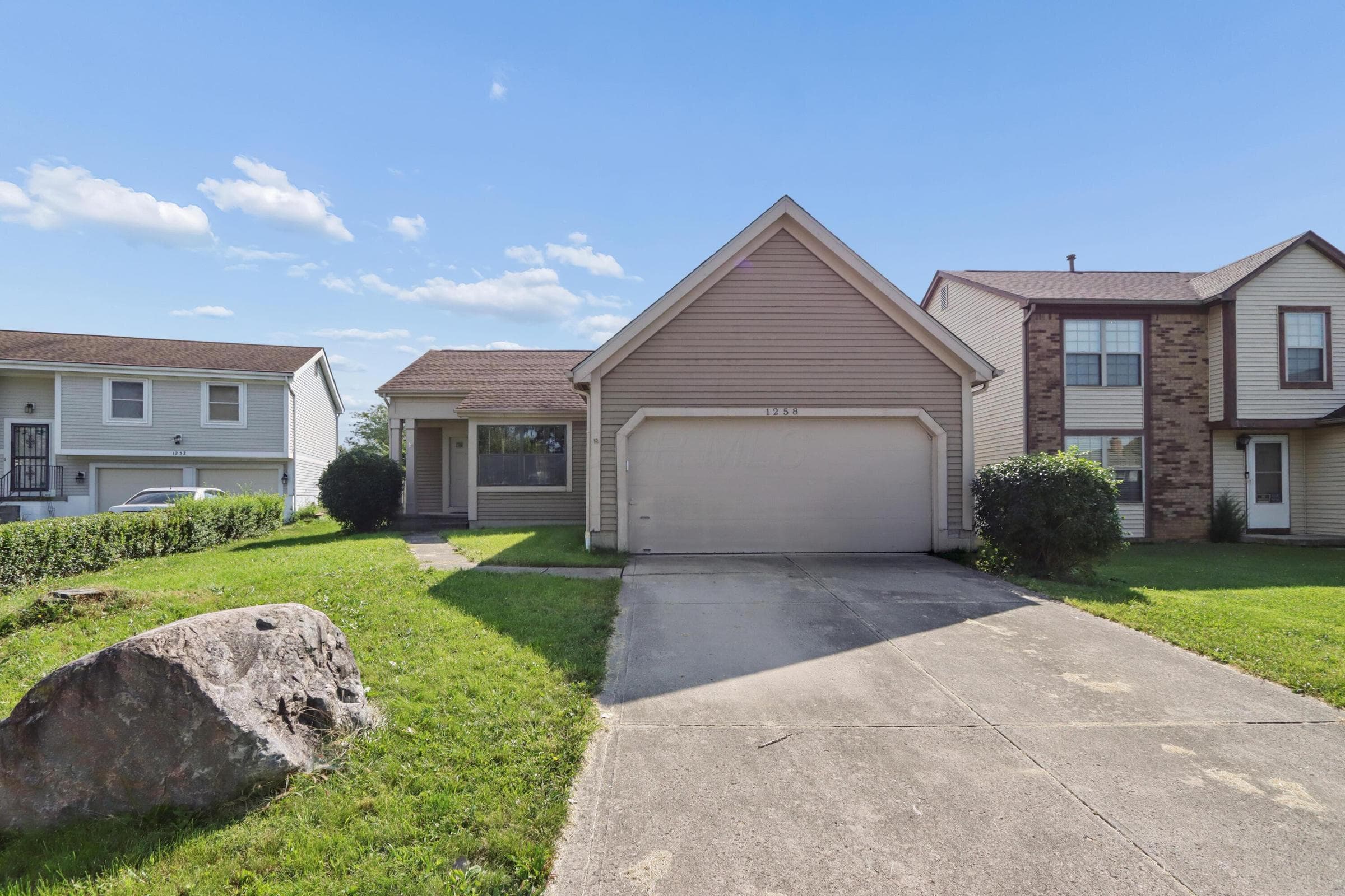 Attached two-car garage, concrete driveway, and front yard with mature landscaping
