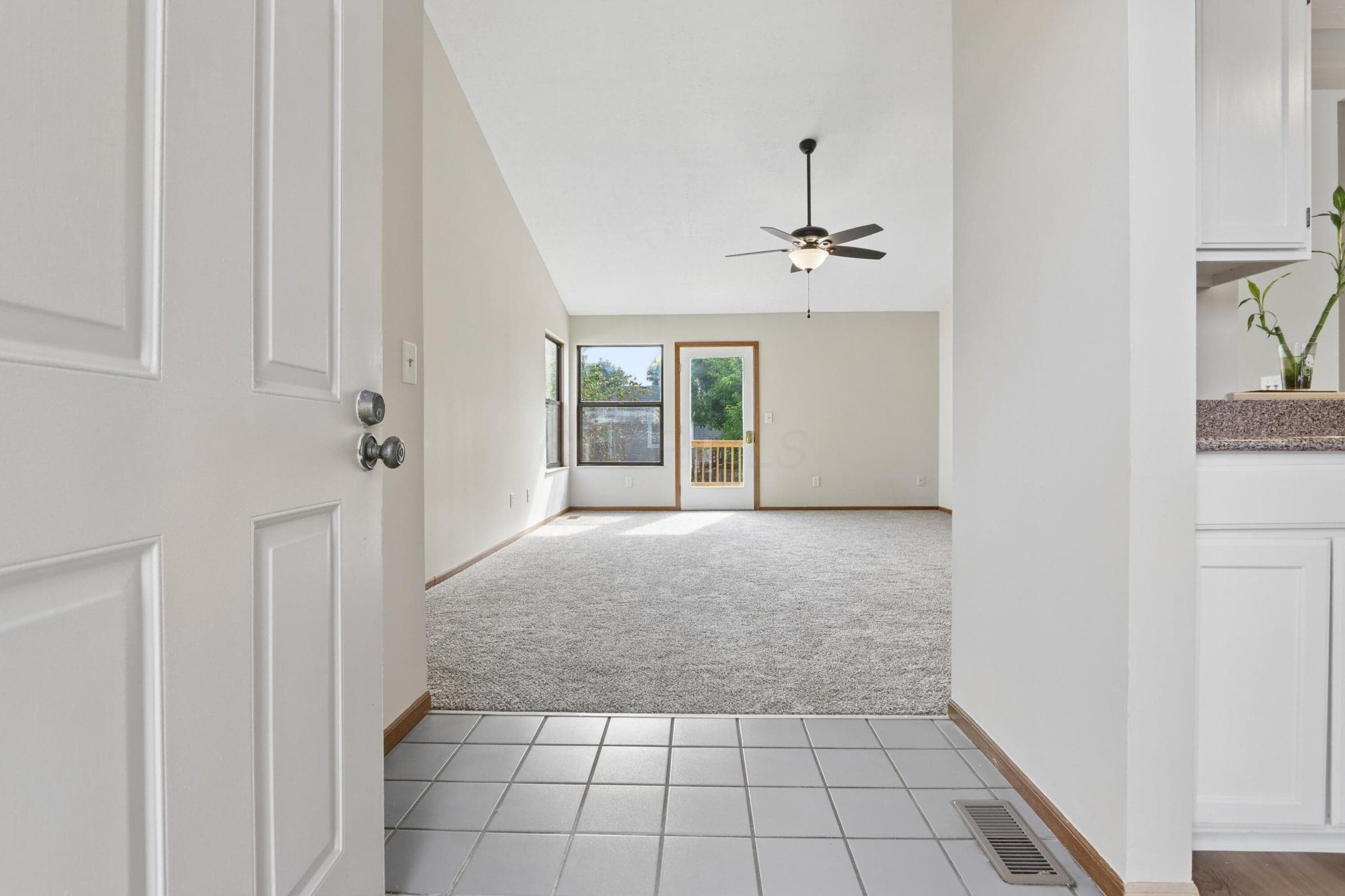 Tiled entry flooring, vaulted ceiling, ceiling fan with integrated lighting, rear patio access, and white kitchen cabinetry