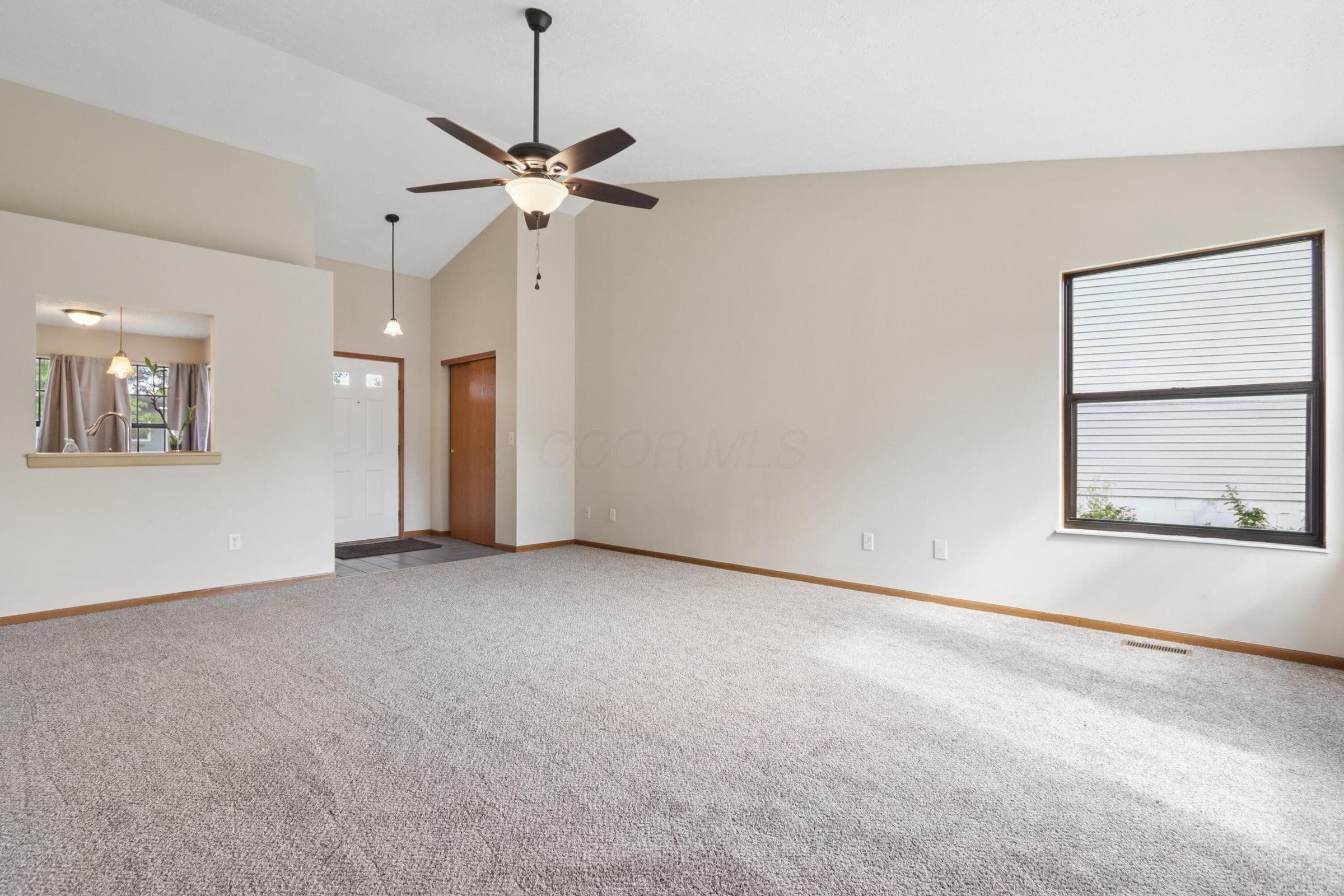 Vaulted ceiling with an attached ceiling fan and light fixture, neutral carpet flooring, and a pass-through window opening