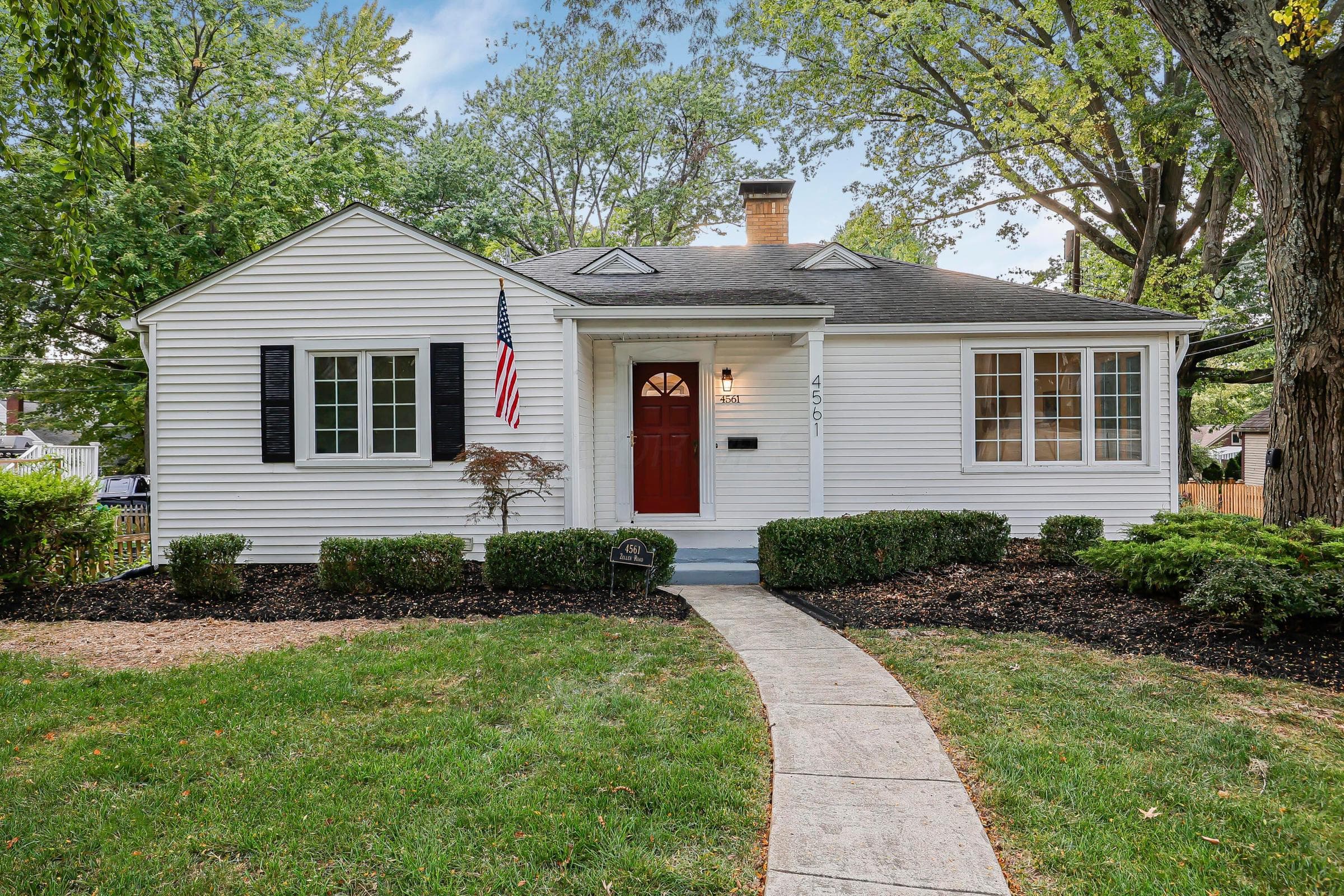 White siding exterior with a red front door, black shutters and American Flag