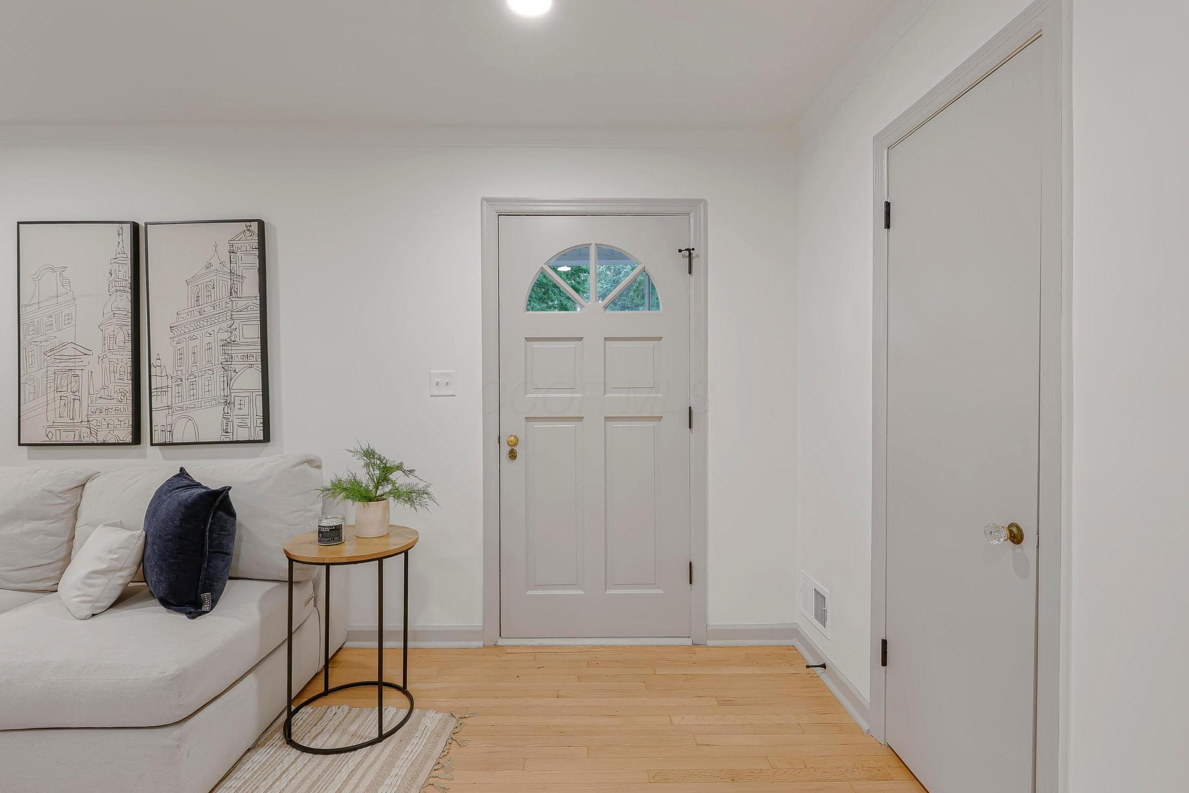 Light wood-finish flooring, recessed lighting, white walls, and a paneled entry door with an arched glass insert