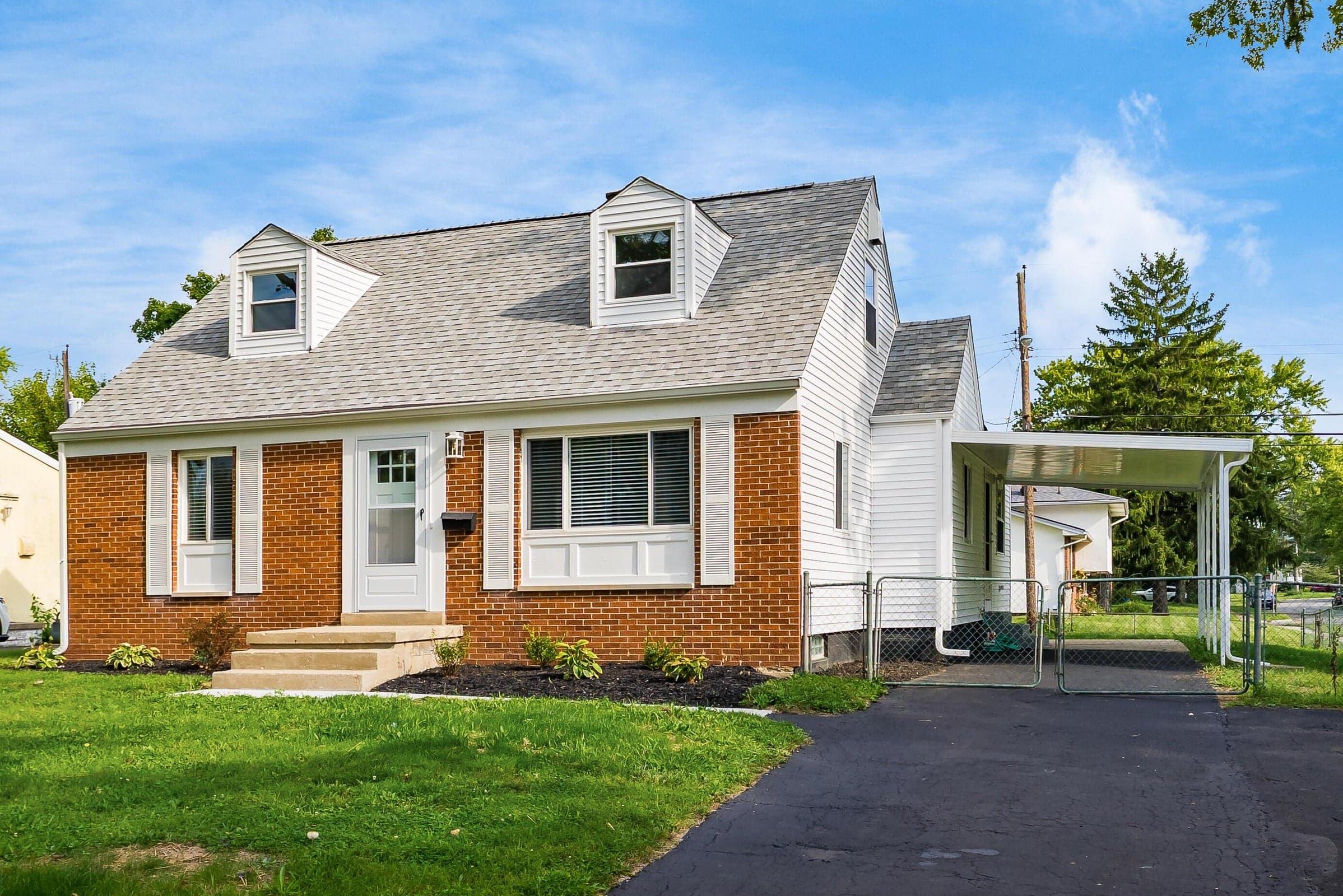 Brick and siding exterior featuring a covered carport, dormer windows, and a manicured lawn