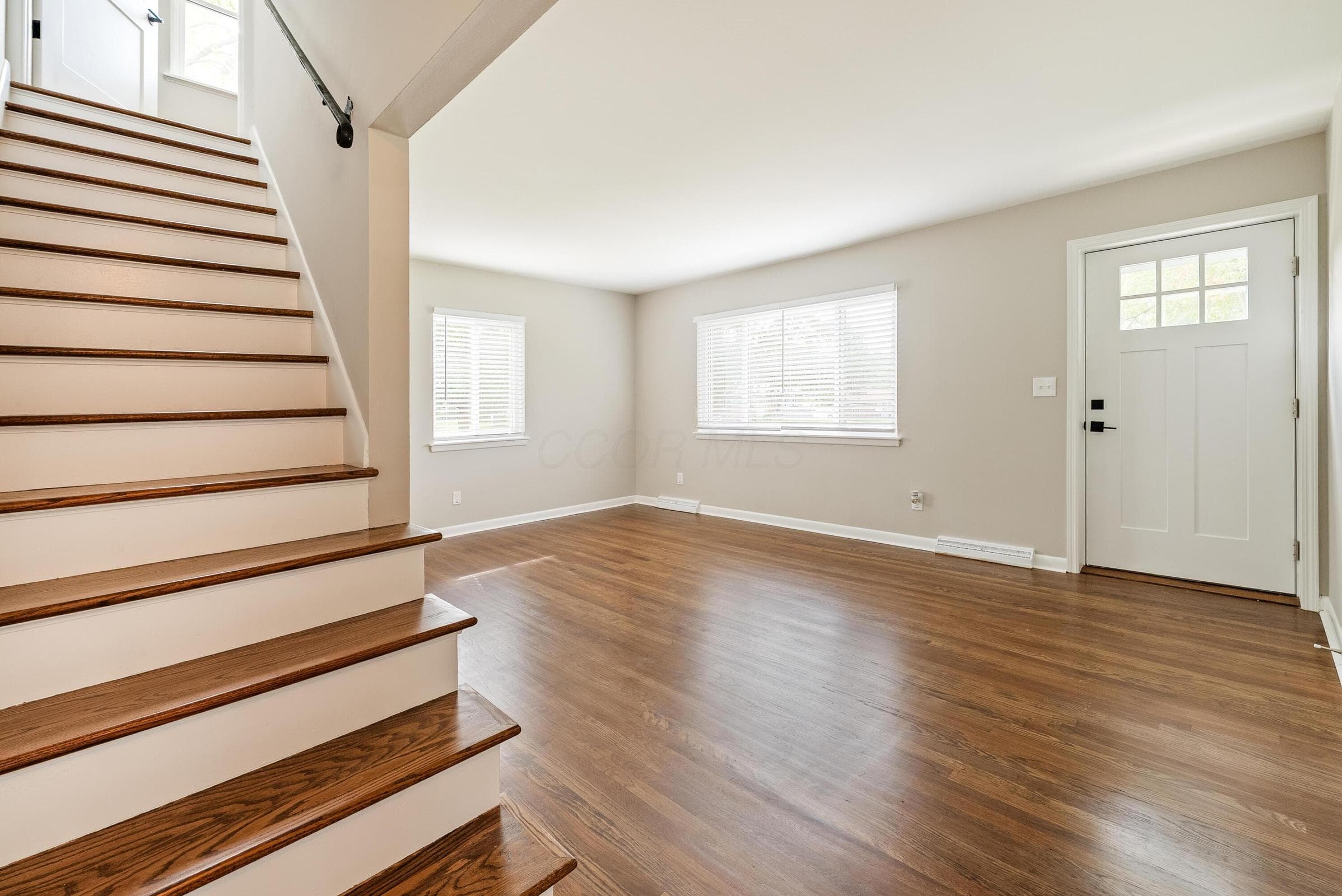Wood-finish flooring throughout, white trim, and a white front entry door with upper window panes