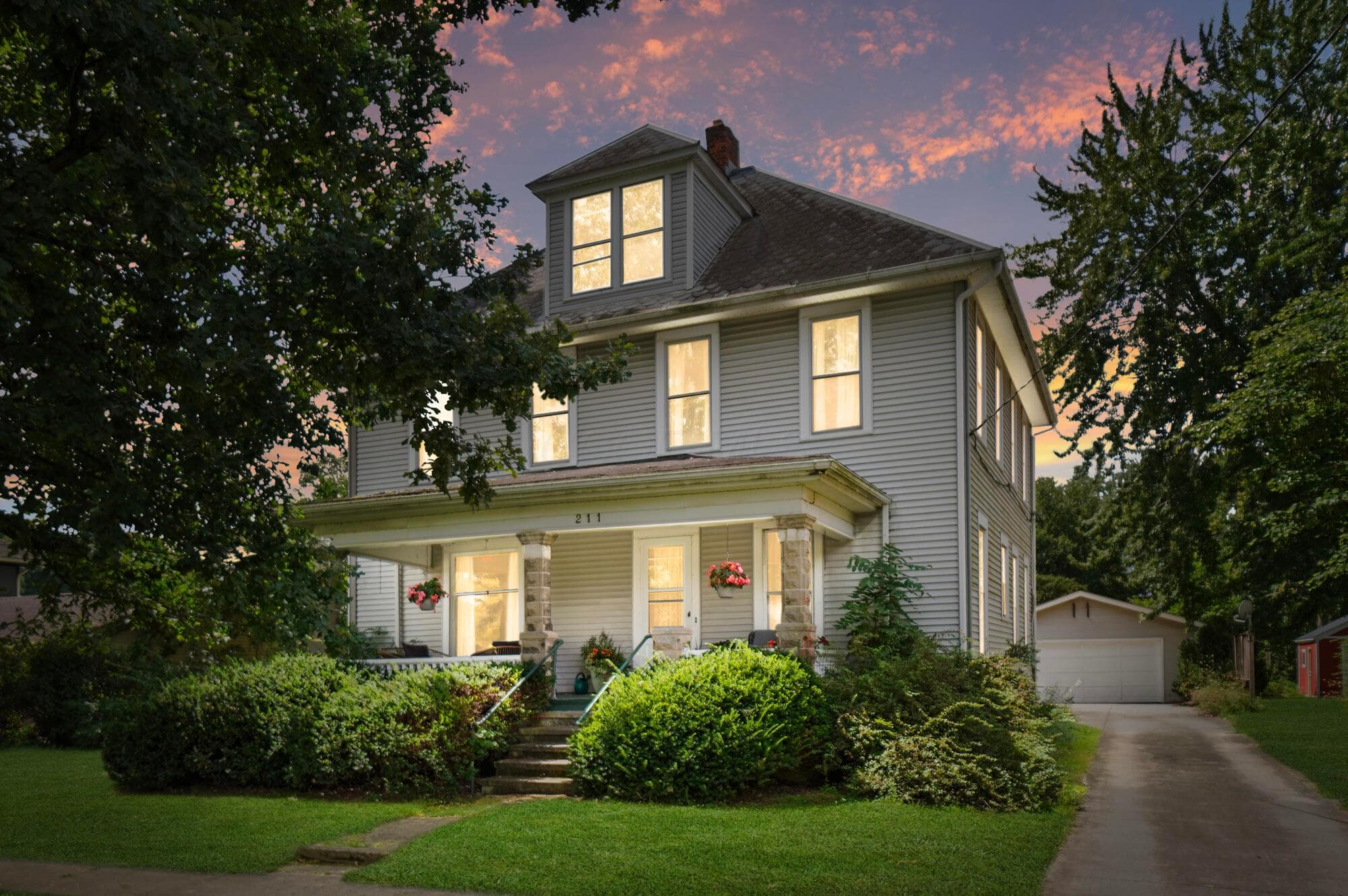 Two-story residence with dormer windows, covered front porch with stone pillars, and a detached garage with a driveway