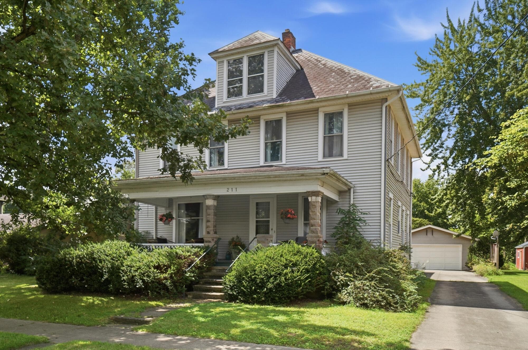 Two-story residence with dormer windows, covered front porch with stone pillars, and a detached garage