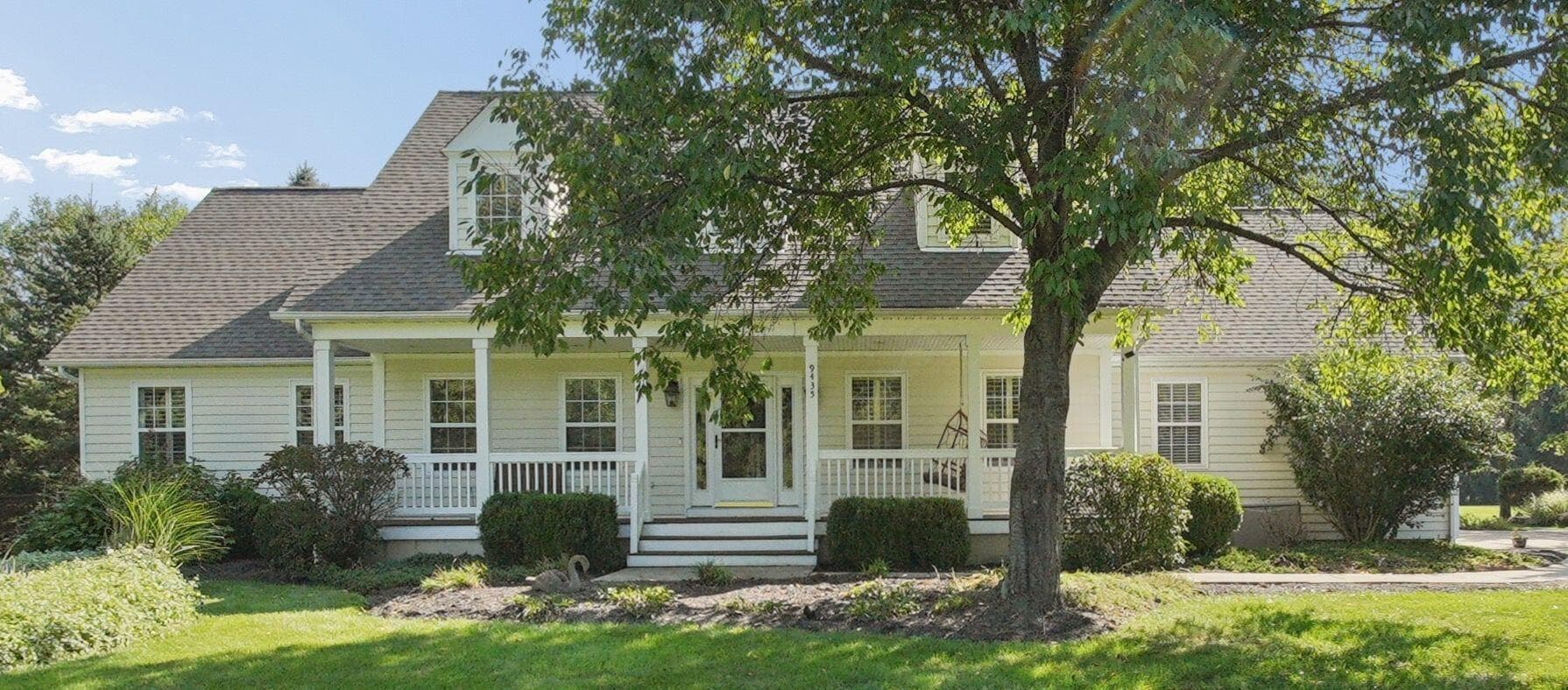 Exterior featuring a covered front porch, white siding, dormer windows, and a mature tree