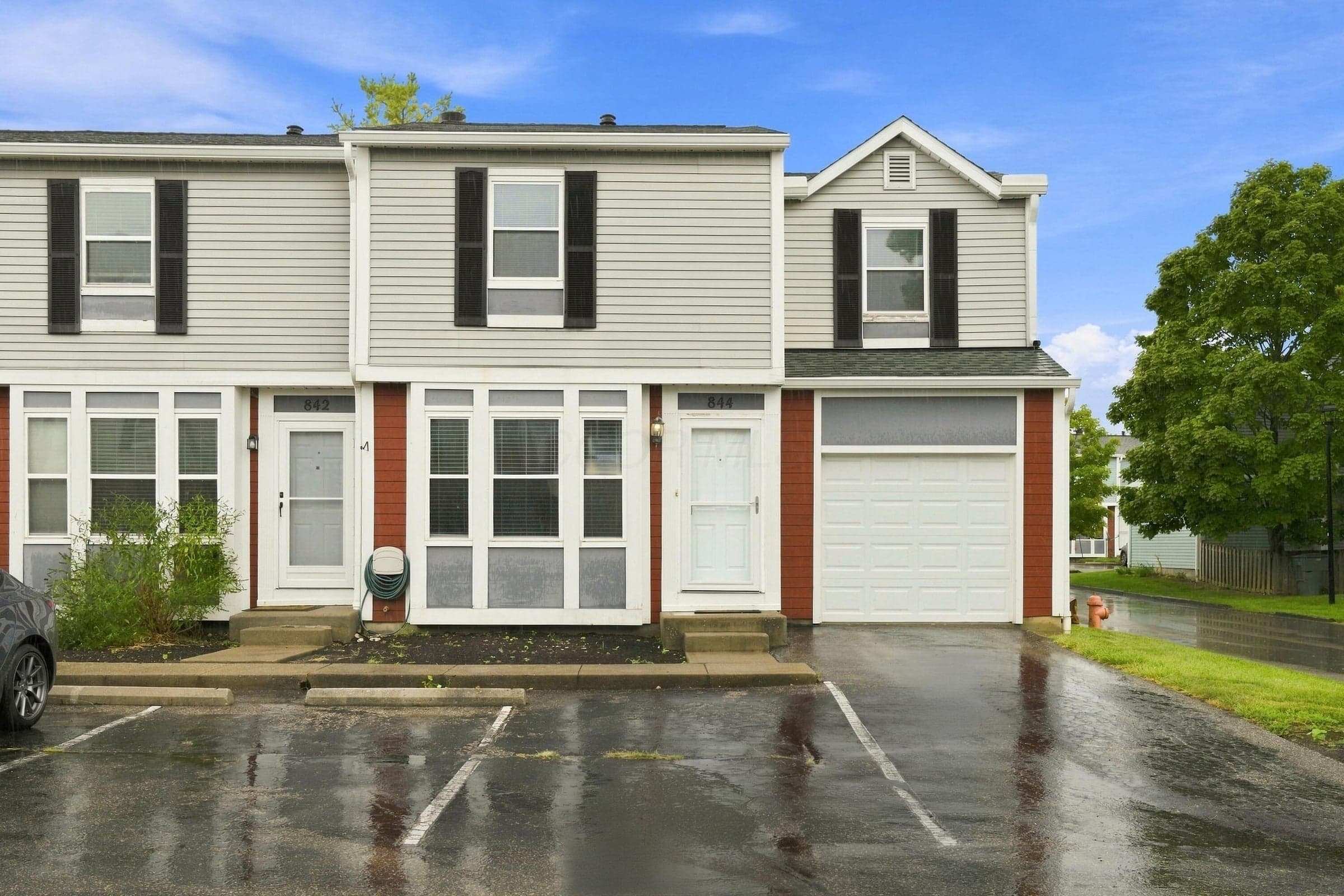 Two-story townhome with light-colored siding and dark shutters, featuring multiple windows