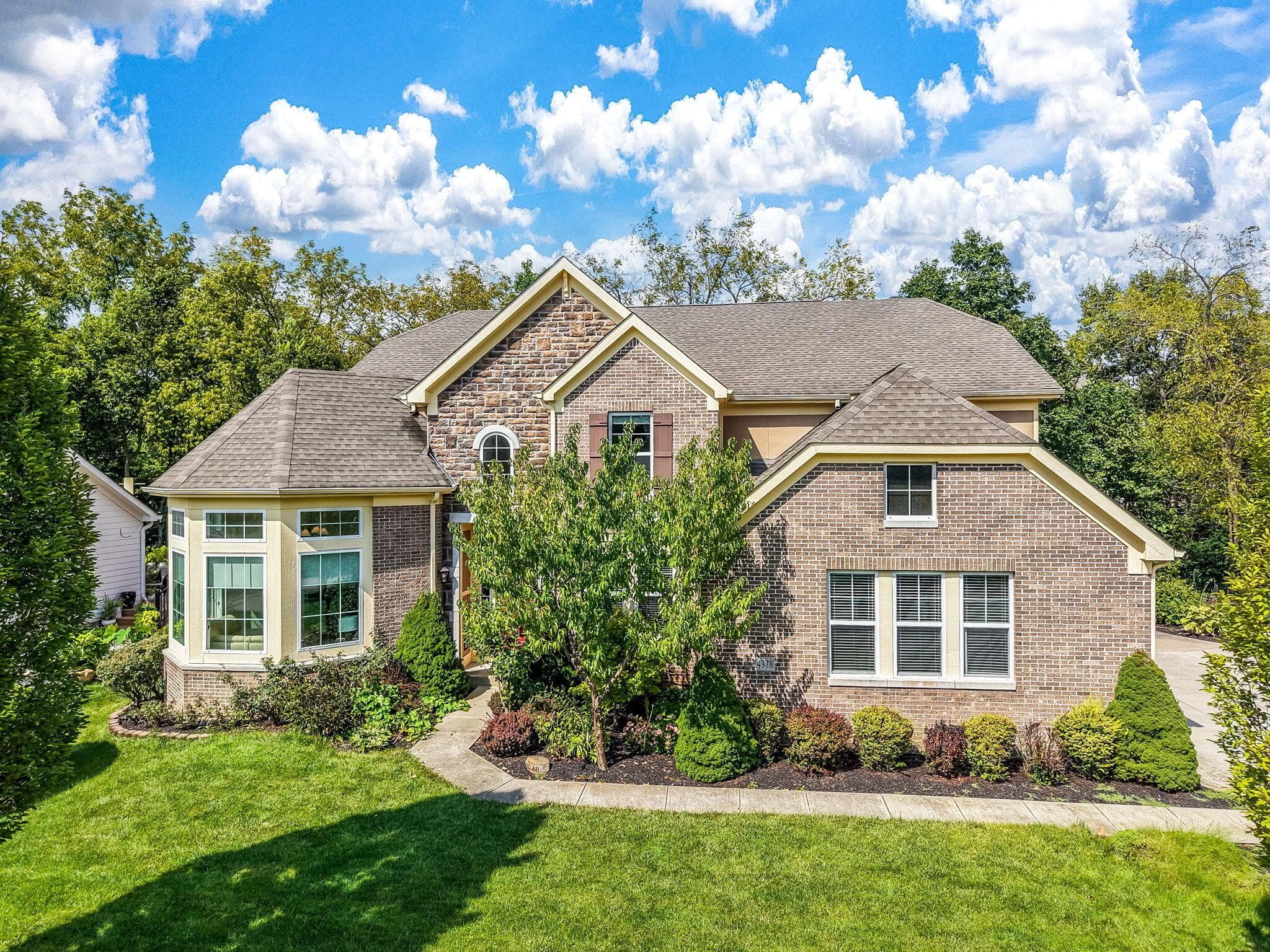 Brick and stone facade, gabled rooflines, bay window, landscaped foundation plantings, and concrete walkway